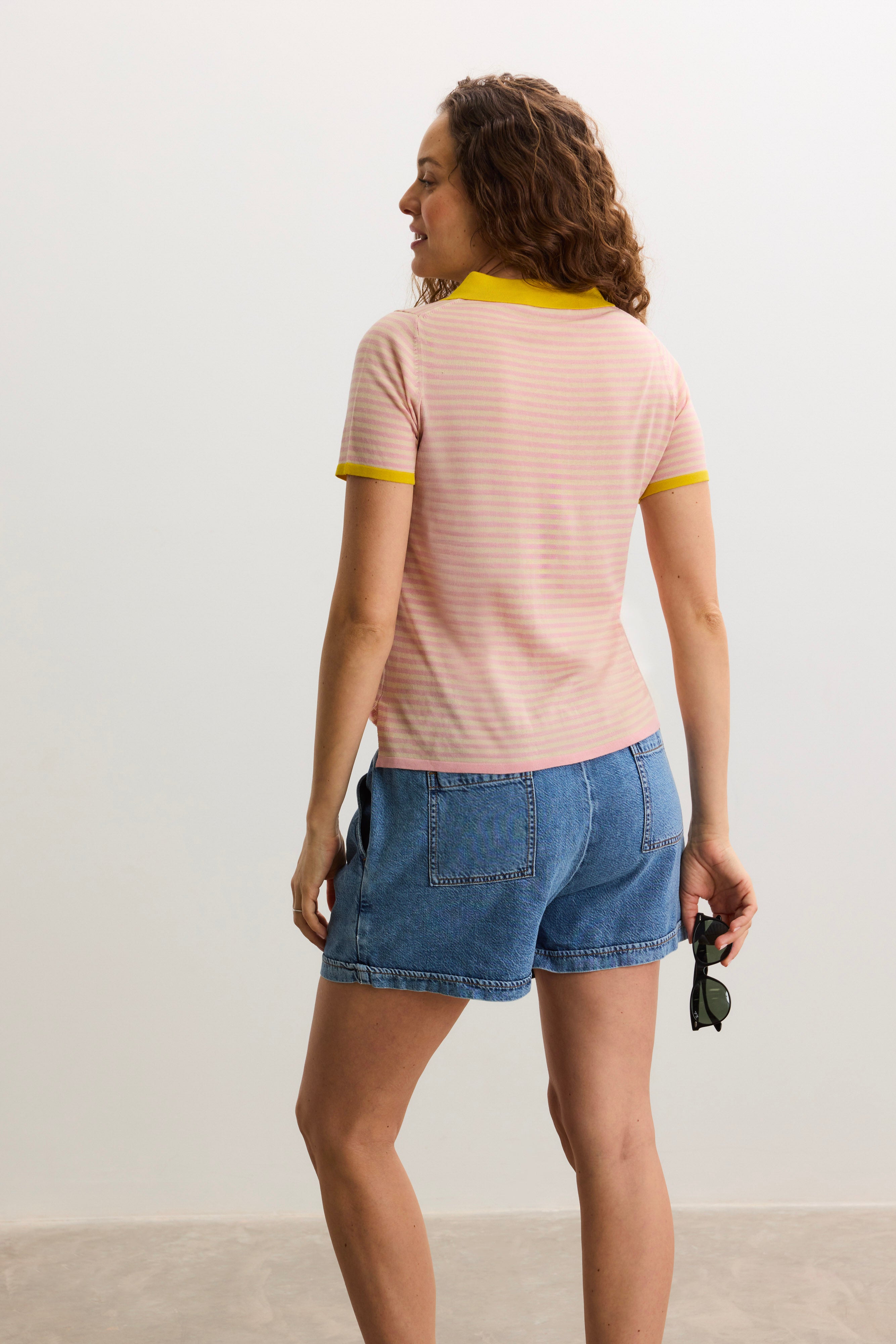 Light pink short-sleeve maternity polo shirt with yellow collar and sleeve trim, worn with denim shorts.