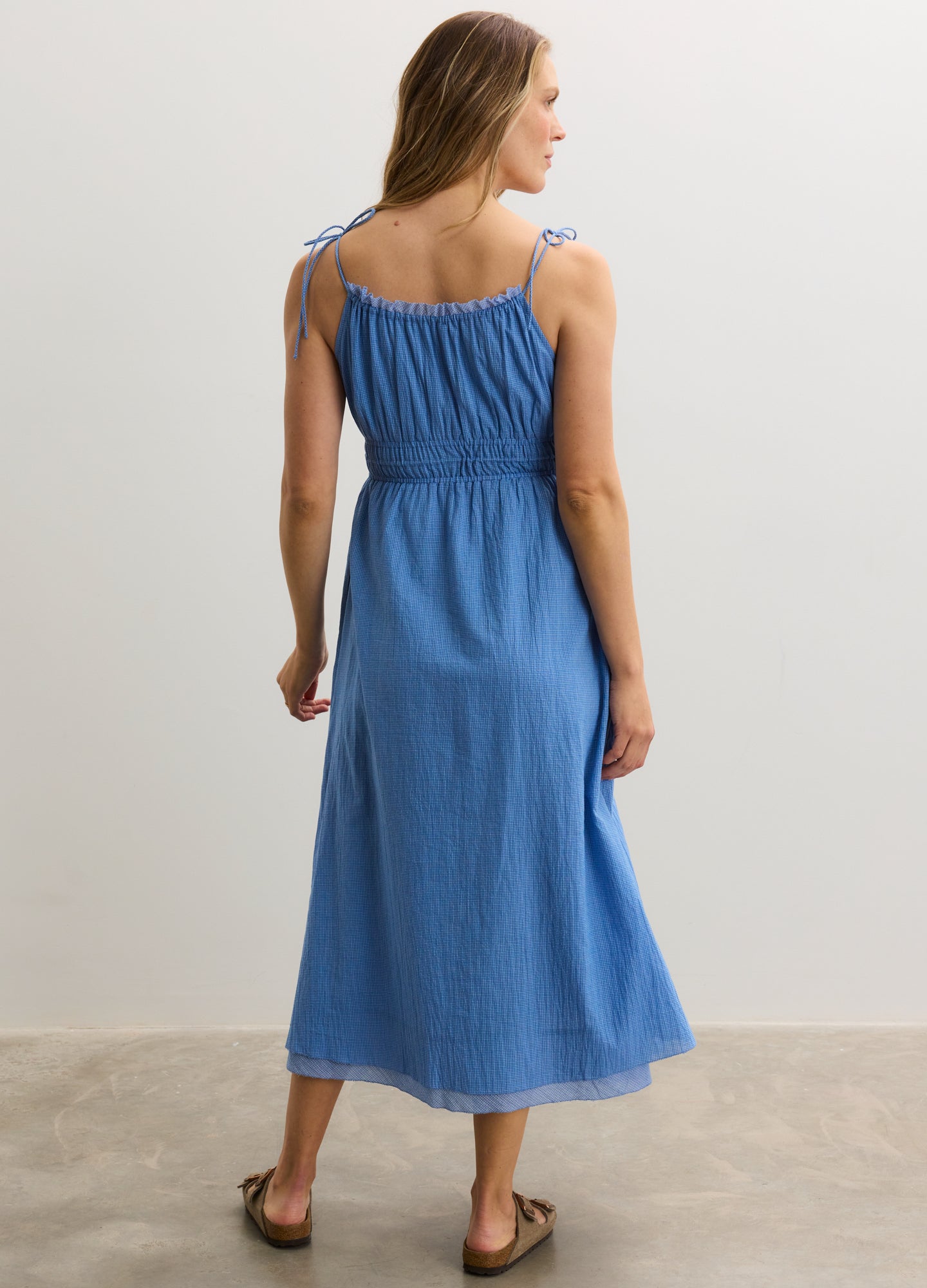 Light blue sleeveless maternity dress with ruched bodice, adjustable tie straps, and flowing midi skirt.