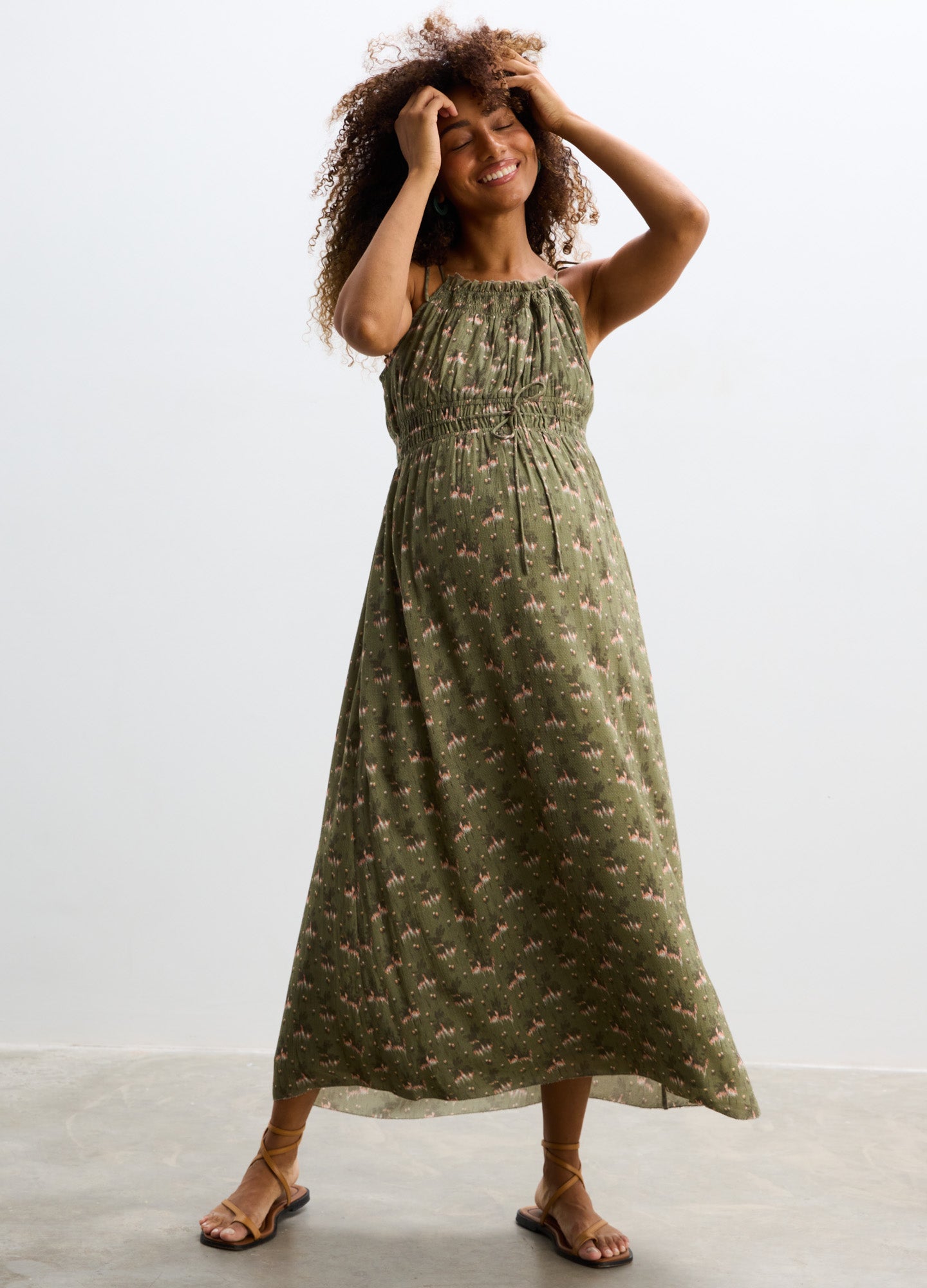 Olive green maternity maxi dress with small floral print, sleeveless with adjustable tie straps and loose, flowing skirt.