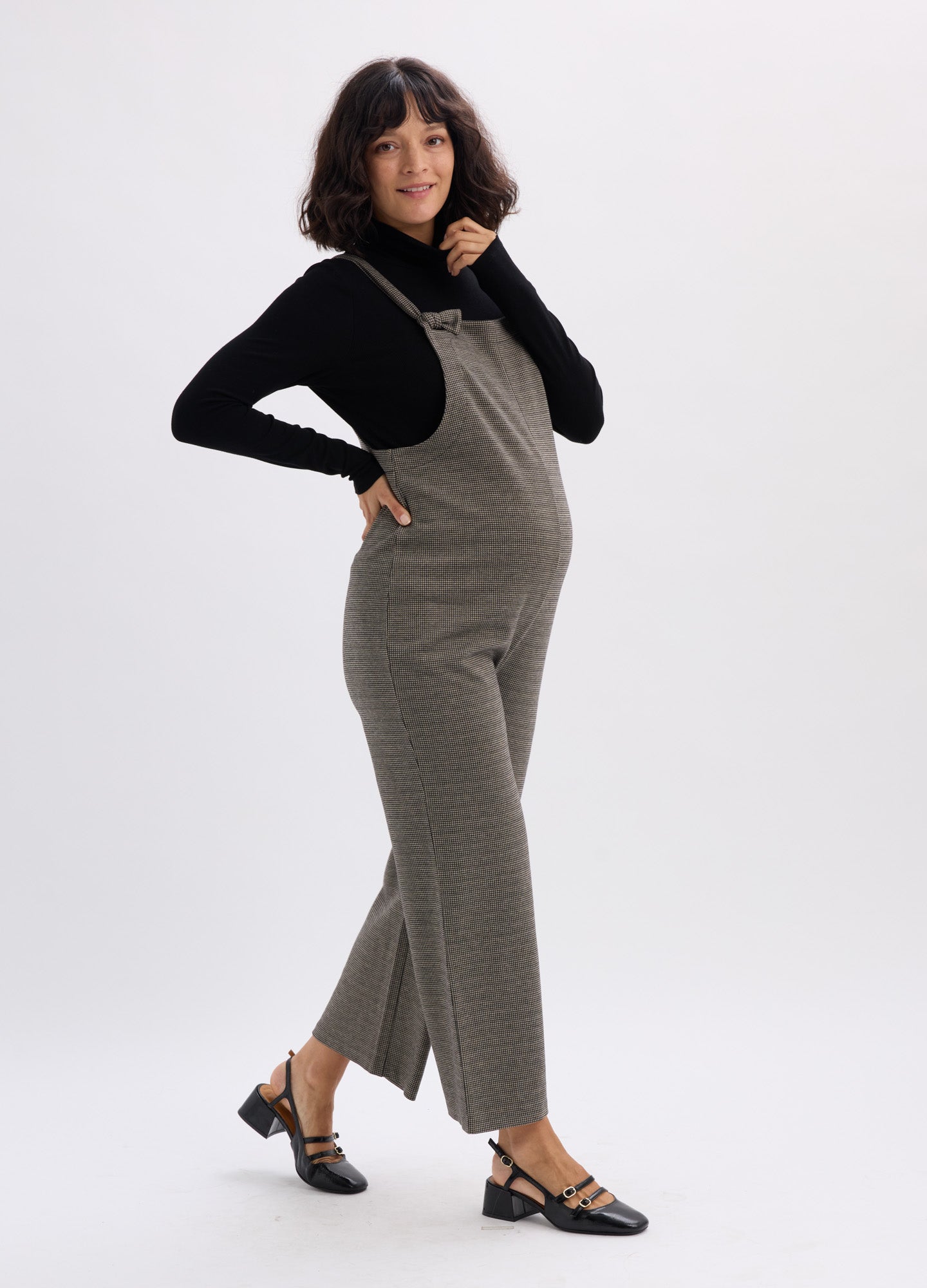 Olive green textured maternity onesie with wide straps, fitted waist, and straight-leg pants paired with a black long-sleeve