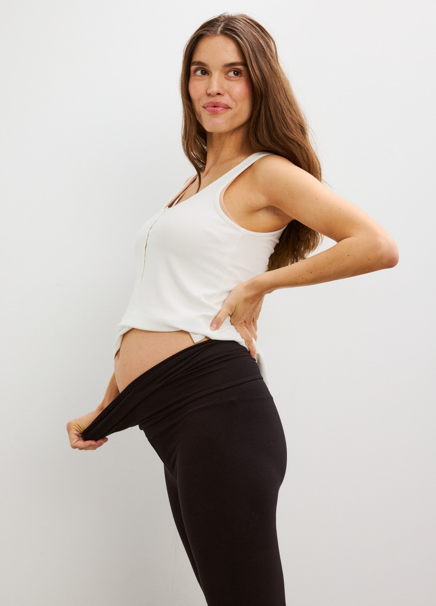 Black stretchy maternity leggings with high, fold-over waistband shown pulled away from belly.
