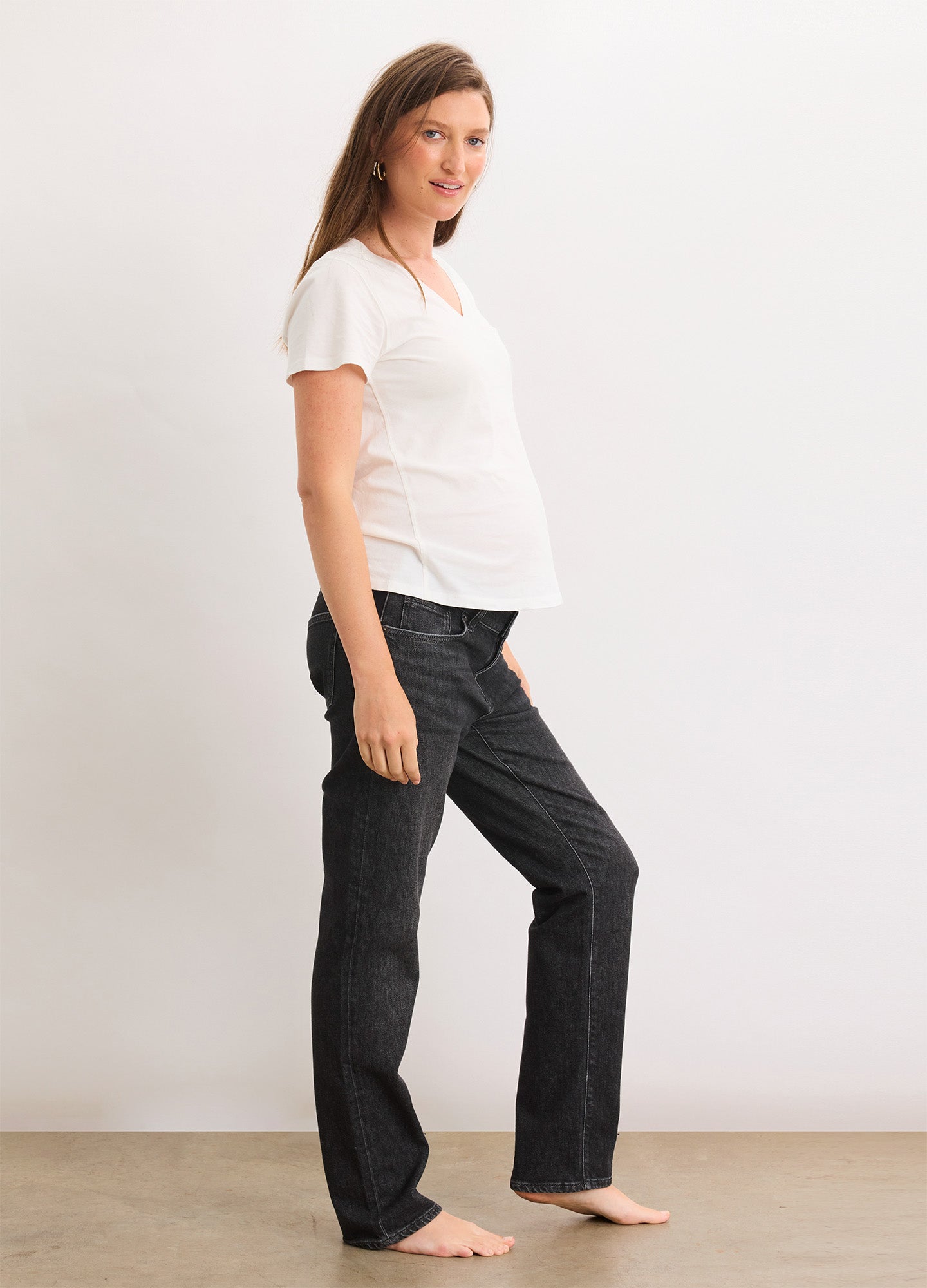 Pregnant woman wearing washed black boyfriend maternity jeans with a relaxed fit and white short-sleeve top.