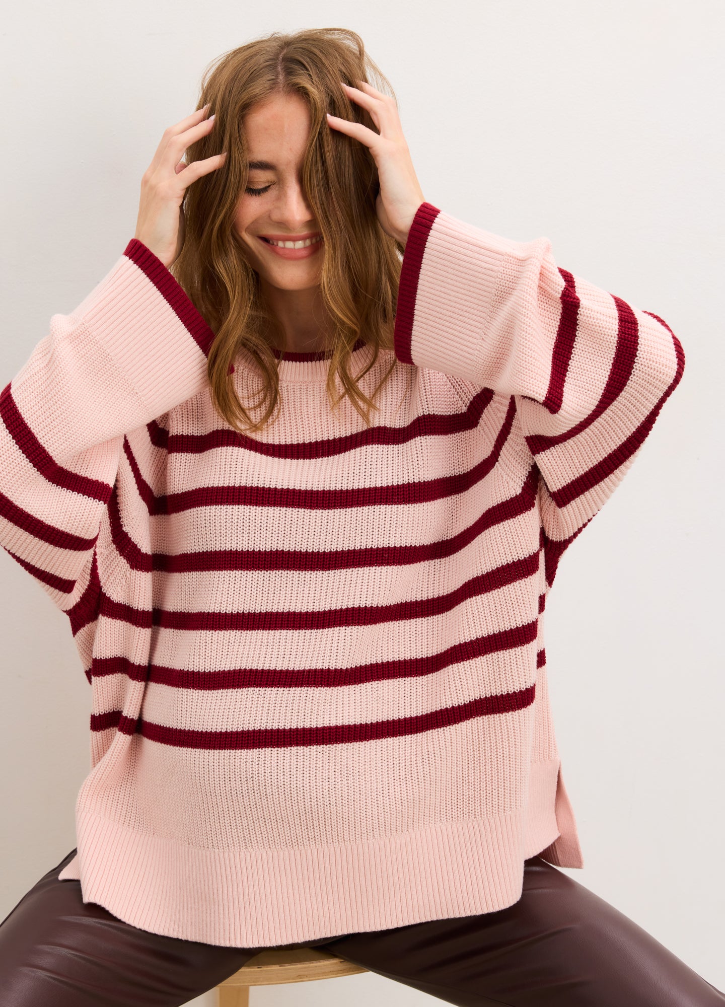 Pregnant woman wearing a pink and red striped sweater against a white background