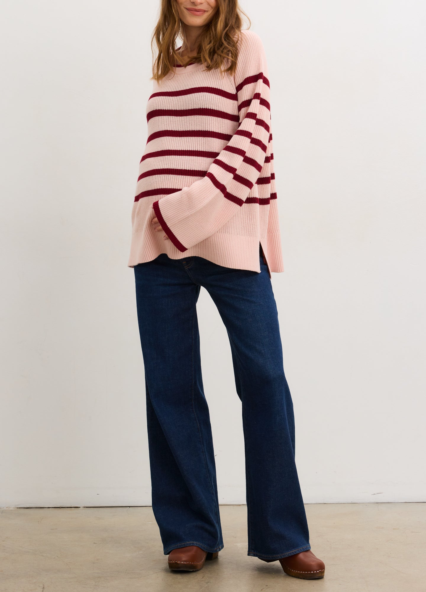 Pregnant woman wearing a pink and red striped sweater against a white background