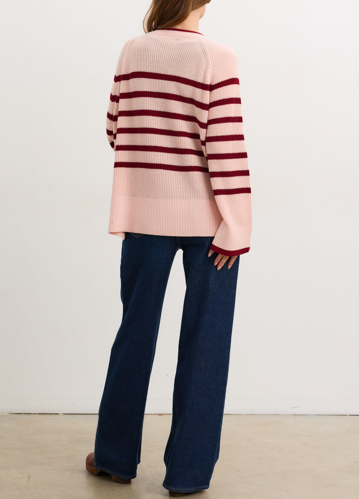 Pregnant woman wearing a pink and red striped sweater against a white background