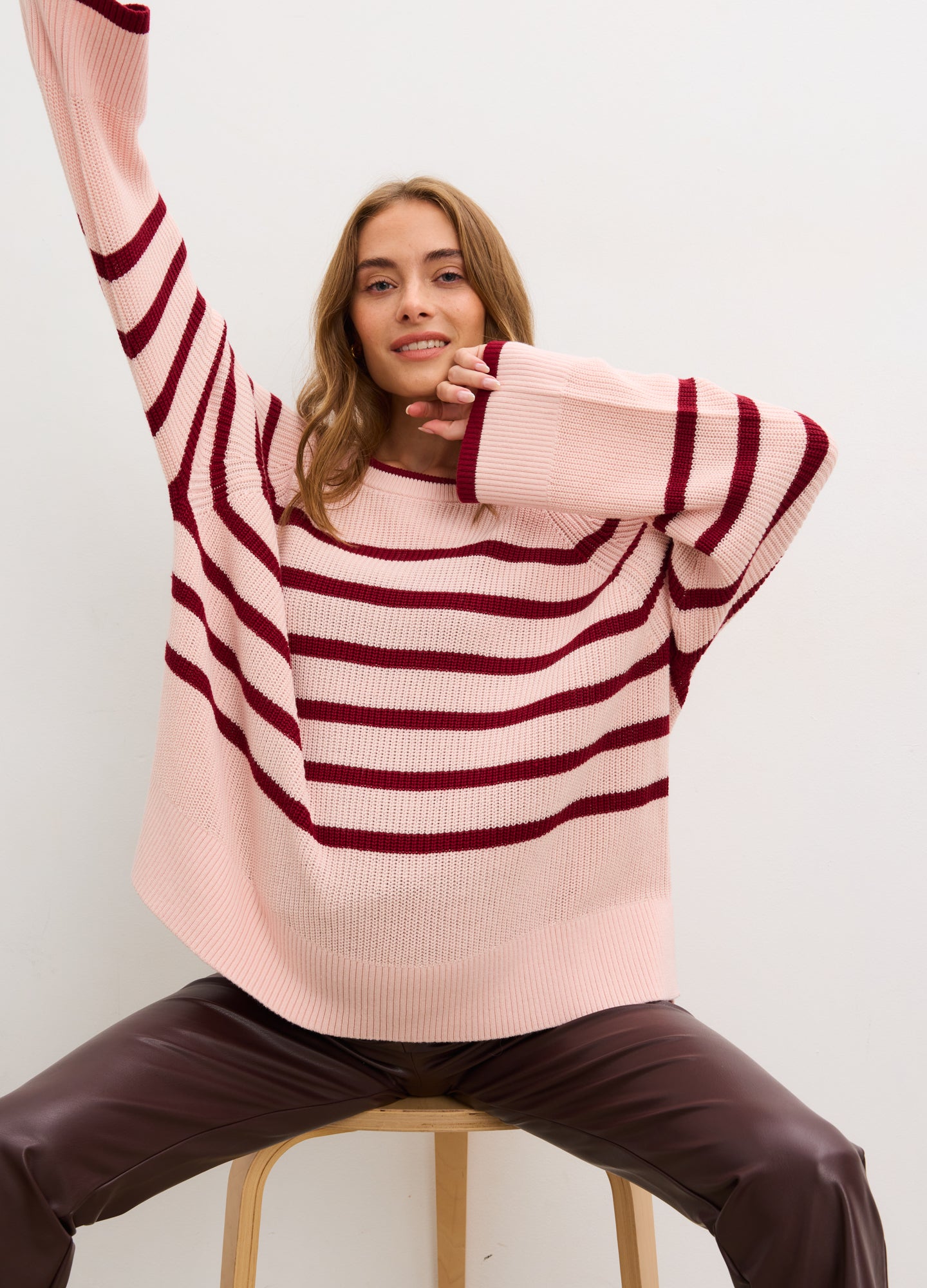 Pregnant woman wearing a pink and red striped sweater against a white background