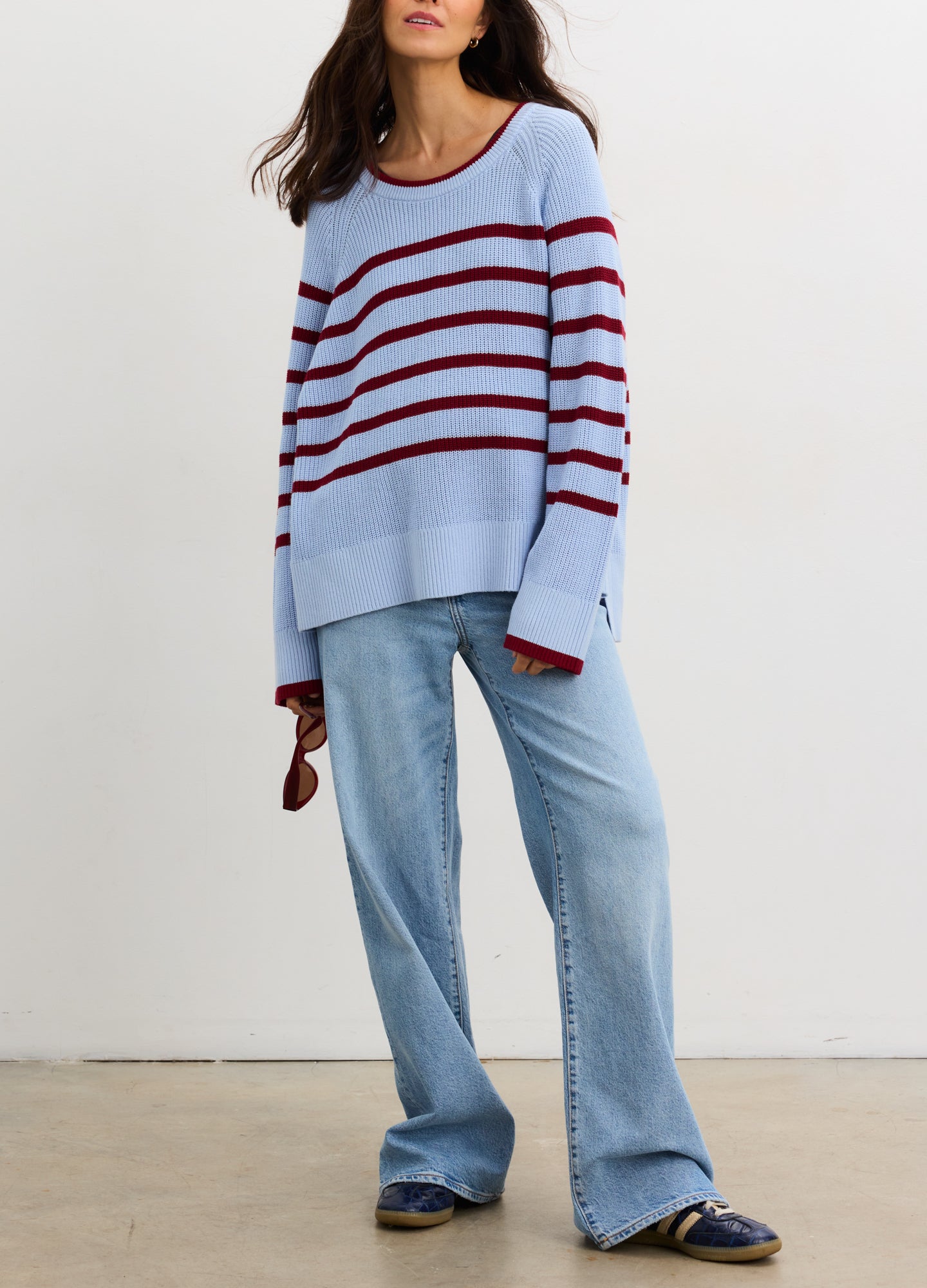 Pregnant woman wearing a blue and red striped sweater with jeans against a plain background