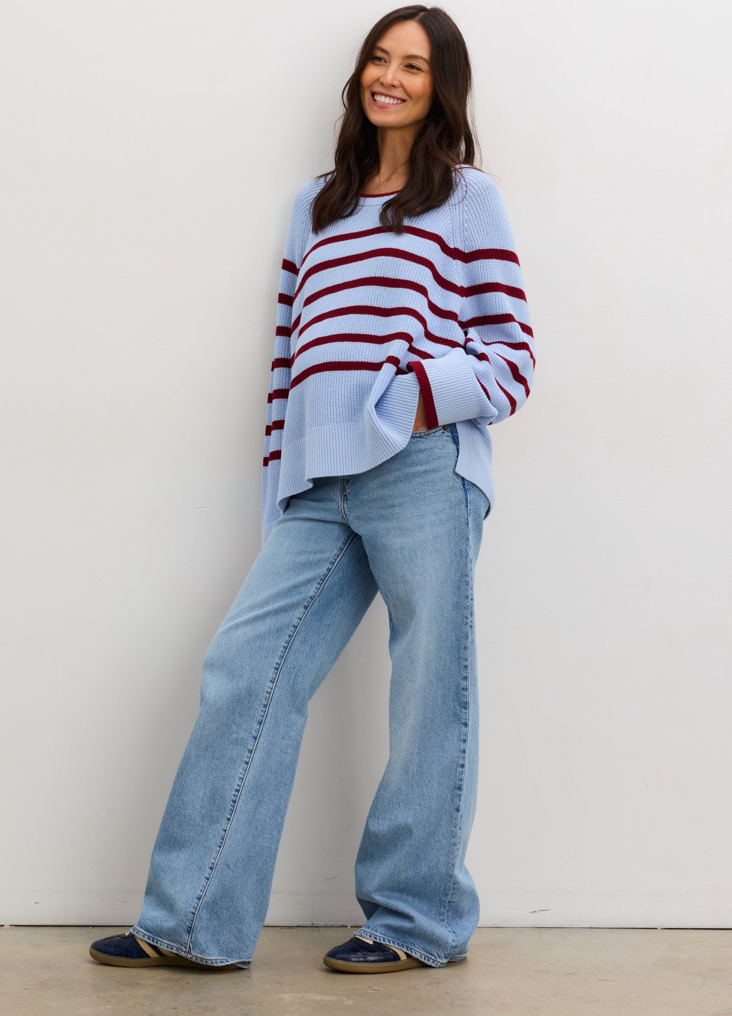 Pregnant woman wearing a blue and red striped sweater with jeans against a plain background