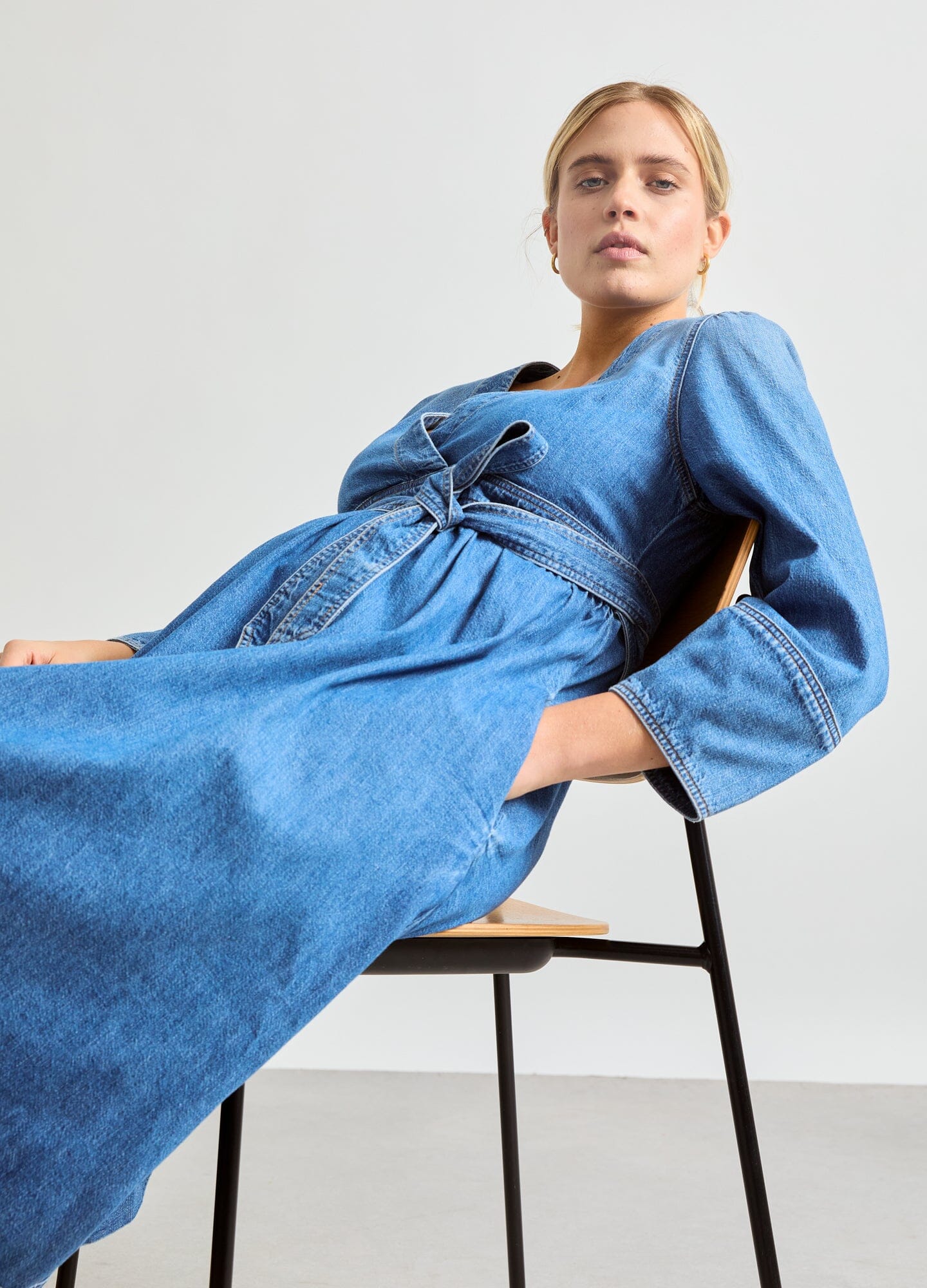 The Denim Carolina Dress - Indigo denim Carolina dress with adjustable waist tie, long sleeves, designed for maternity, nursing, and postpartum wear.