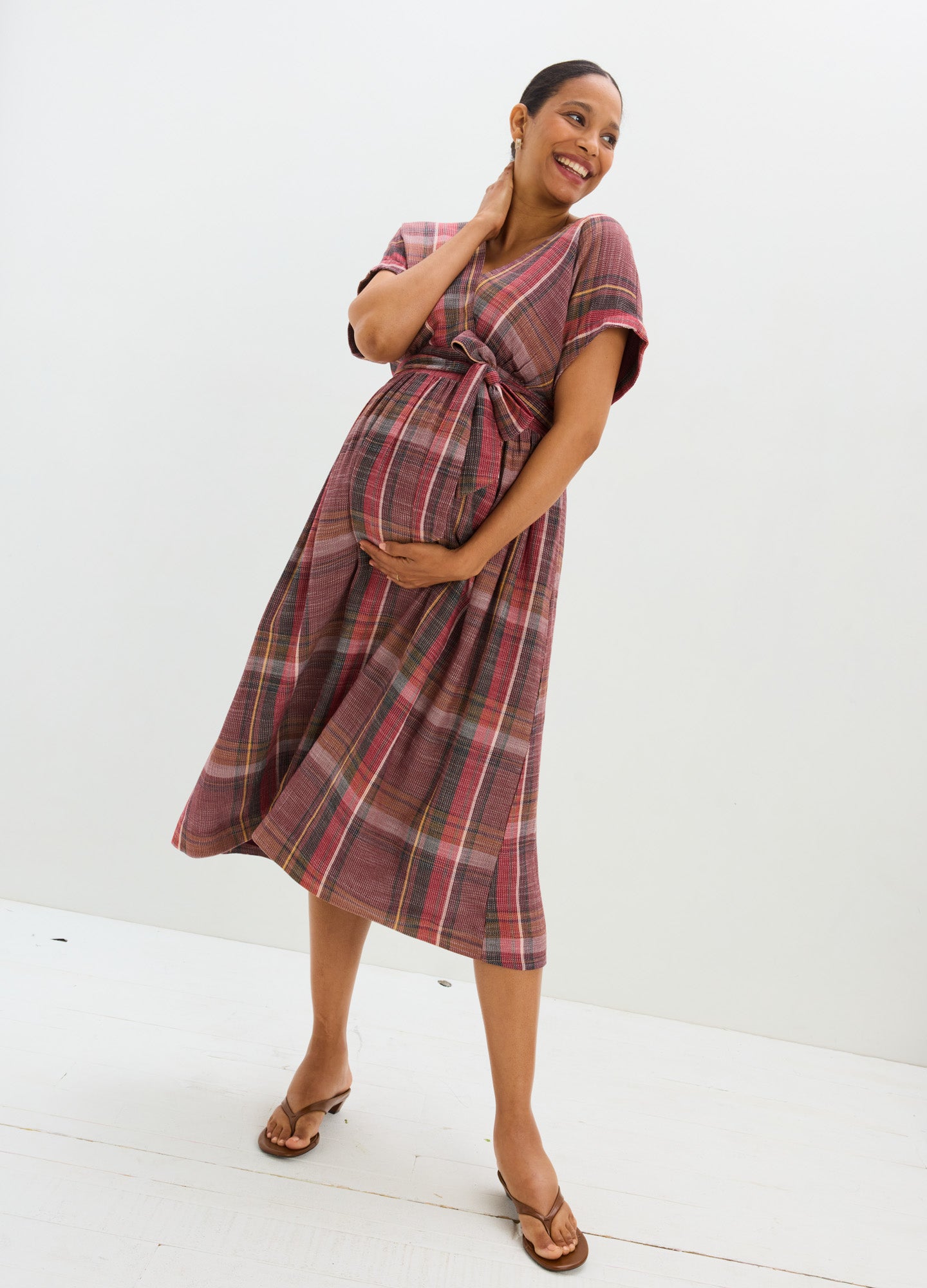 Plaid maternity dress with short sleeves, V-neckline, and empire waist in warm red and brown tones.