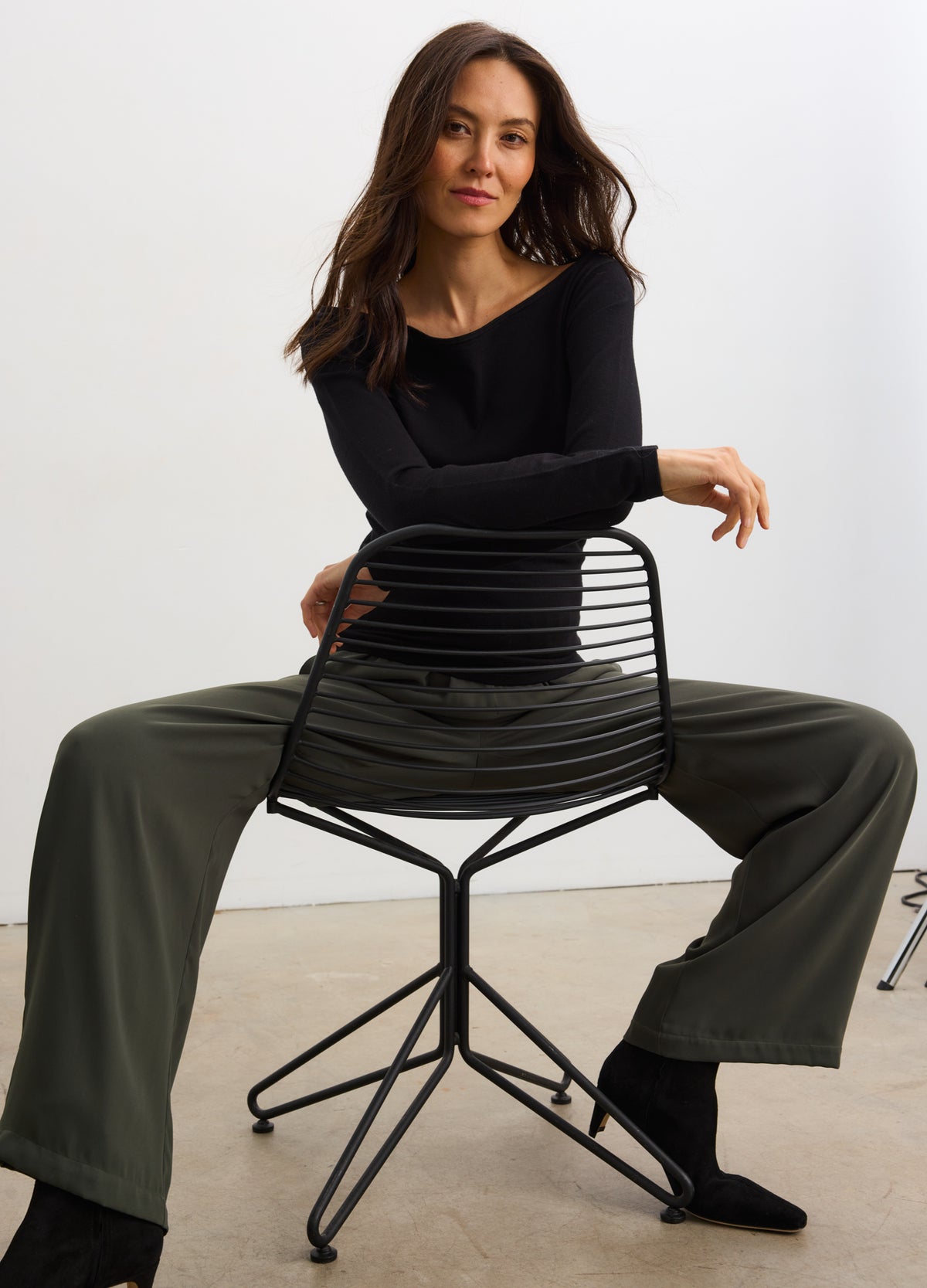 Pregnant woman wearing basil green drapey maternity pull-on pants with elastic waistband and wide legs.