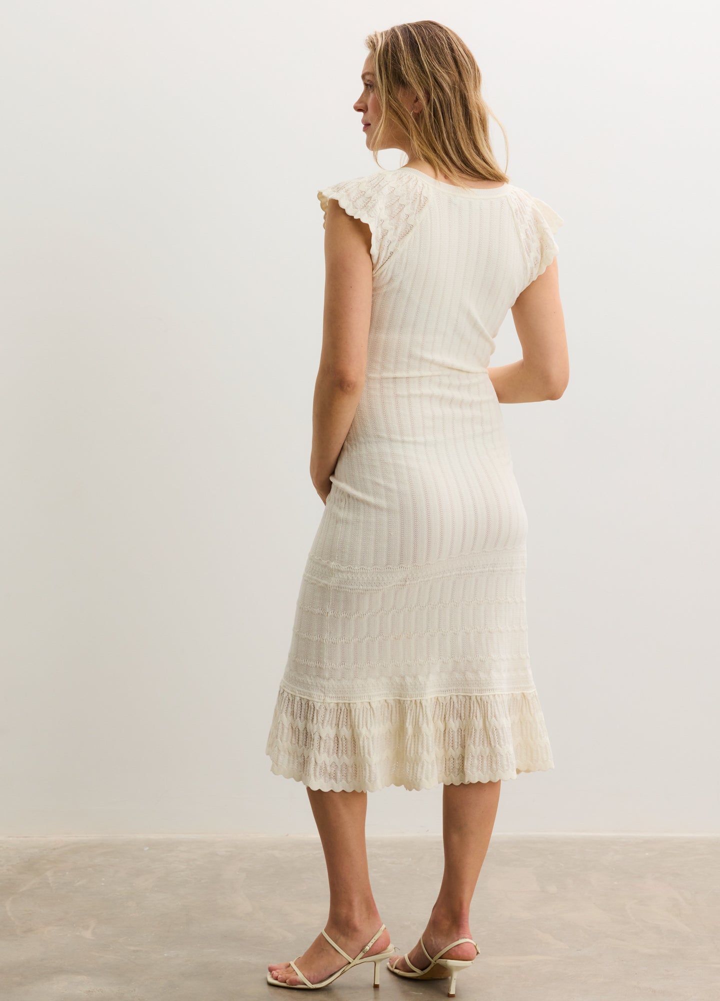 Cream ribbed knit maternity dress with cap sleeves and ruffled hem, knee-length fit.