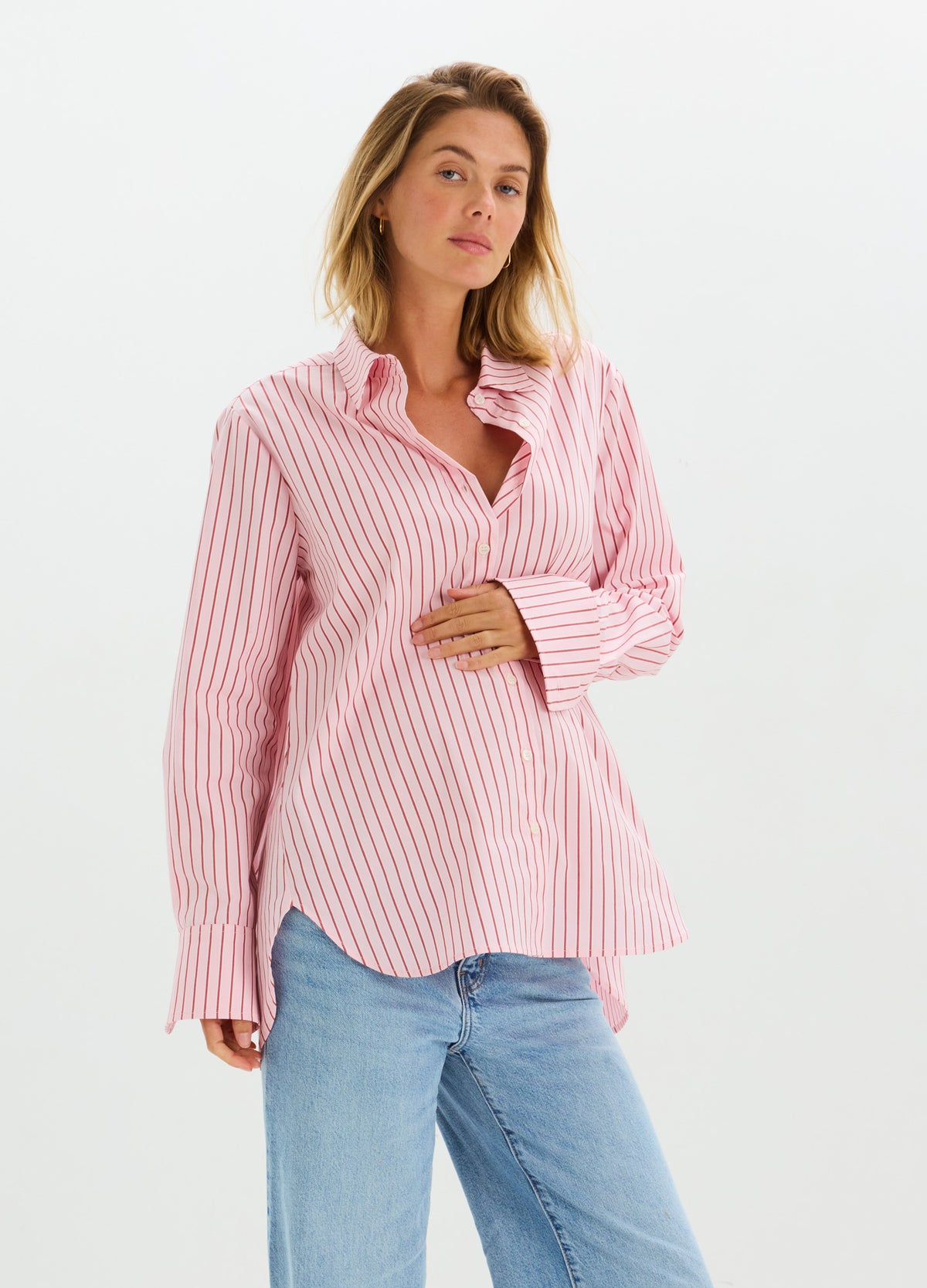 Pink and white striped long-sleeve maternity button-down shirt with relaxed fit, worn with blue jeans.
