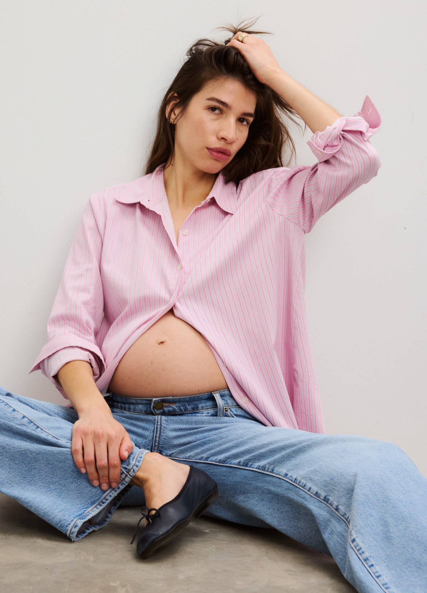 Light pink maternity button-down shirt with long sleeves paired with light blue jeans and black flats.
