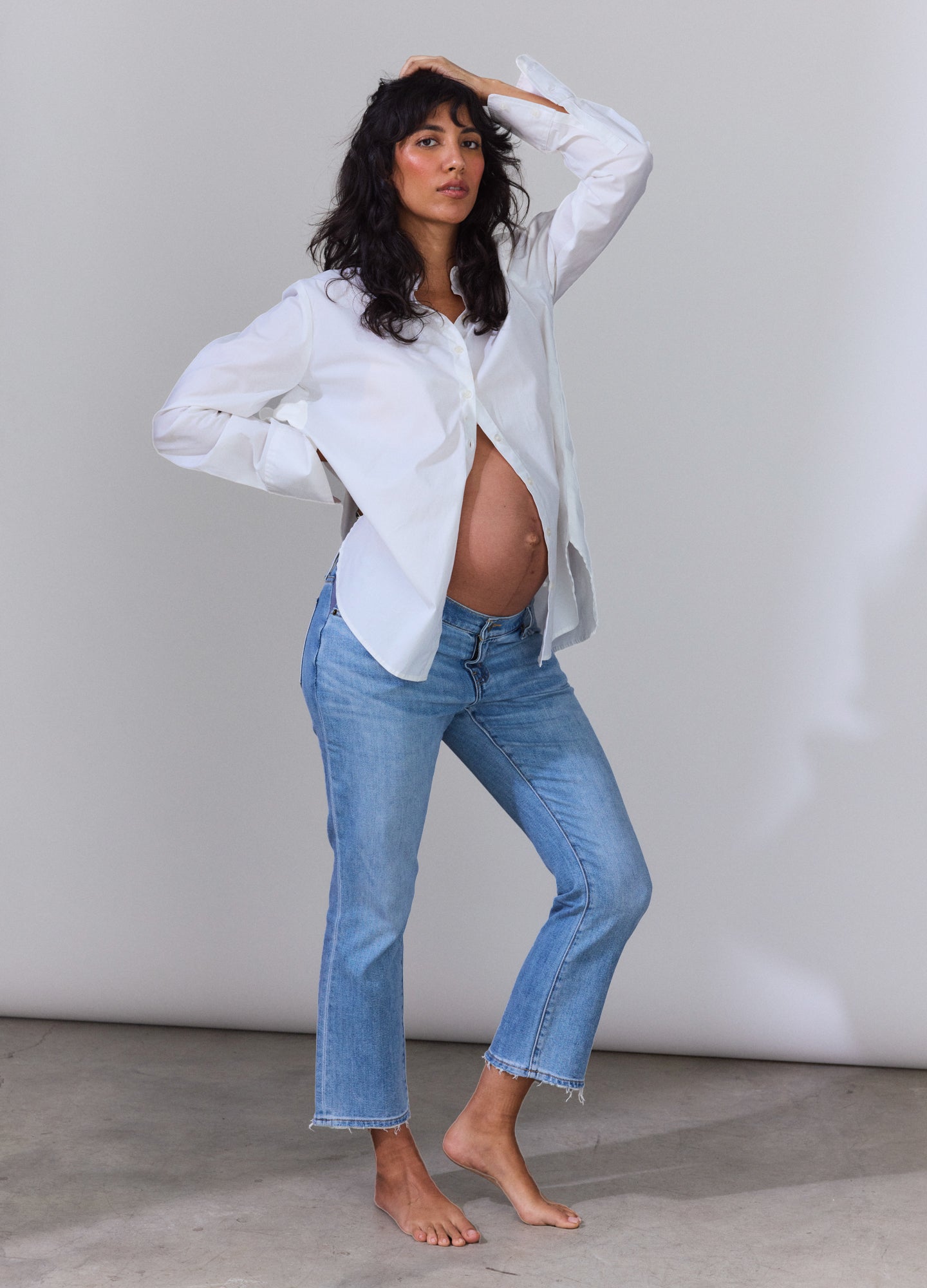 Loose white cotton button-down shirt paired with light blue cropped jeans on a pregnant model.
