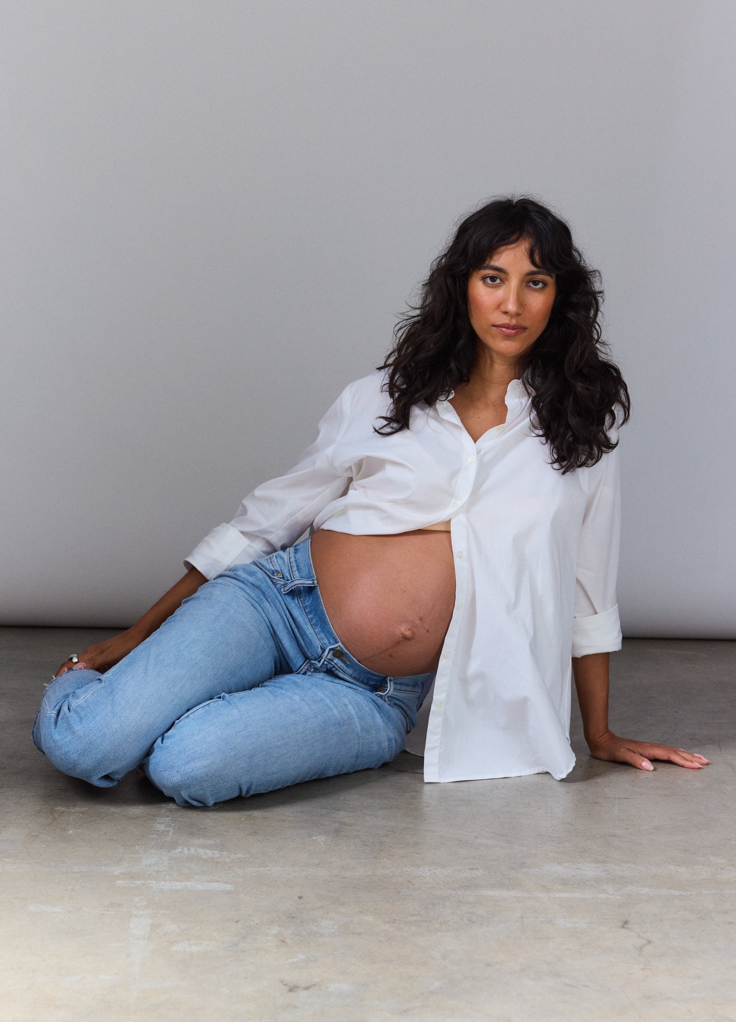 White long-sleeve buttondown shirt with relaxed fit tailored for maternity, paired with light blue jeans.