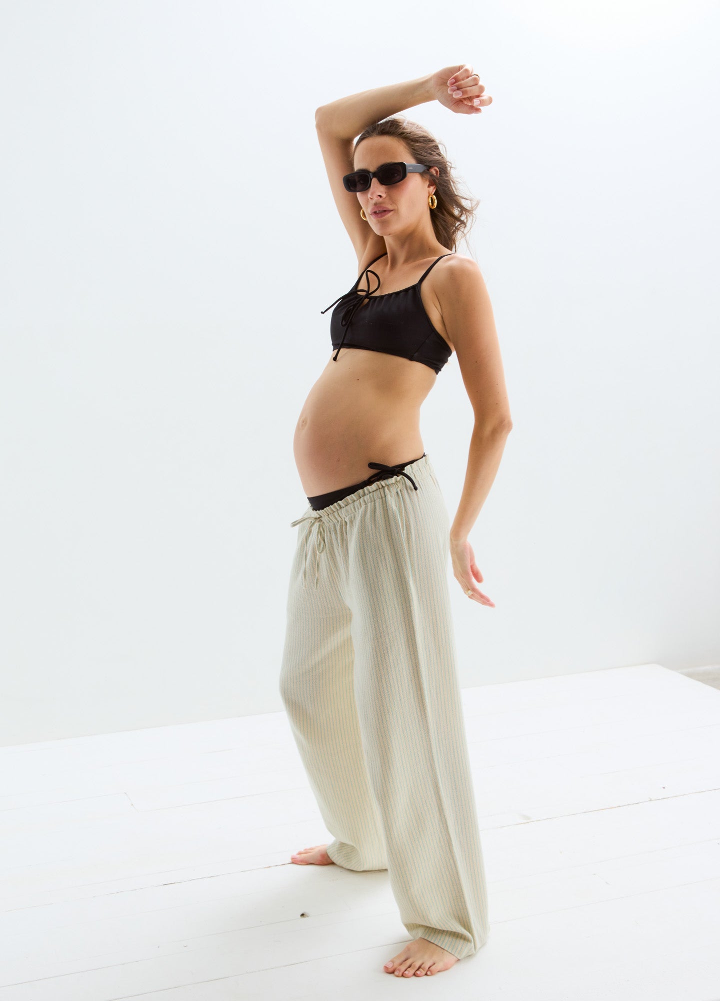 Black maternity bikini top with adjustable tie front, paired with loose beige wide-leg pants and sunglasses.