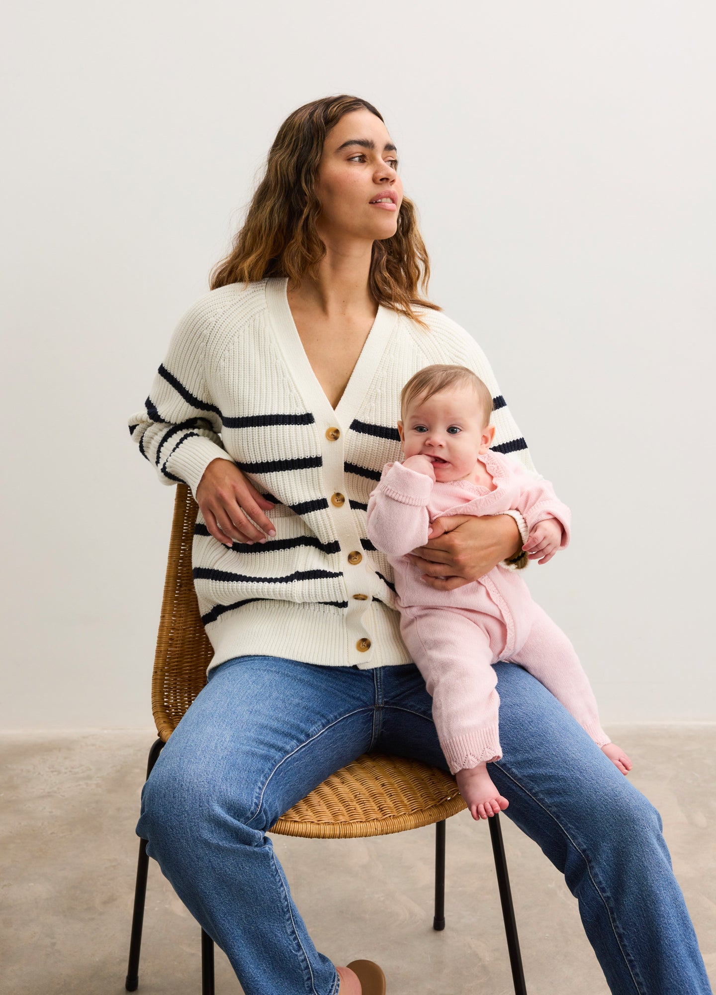 Cream-colored knit cardigan with black stripes and buttons, worn open over maternity jeans.