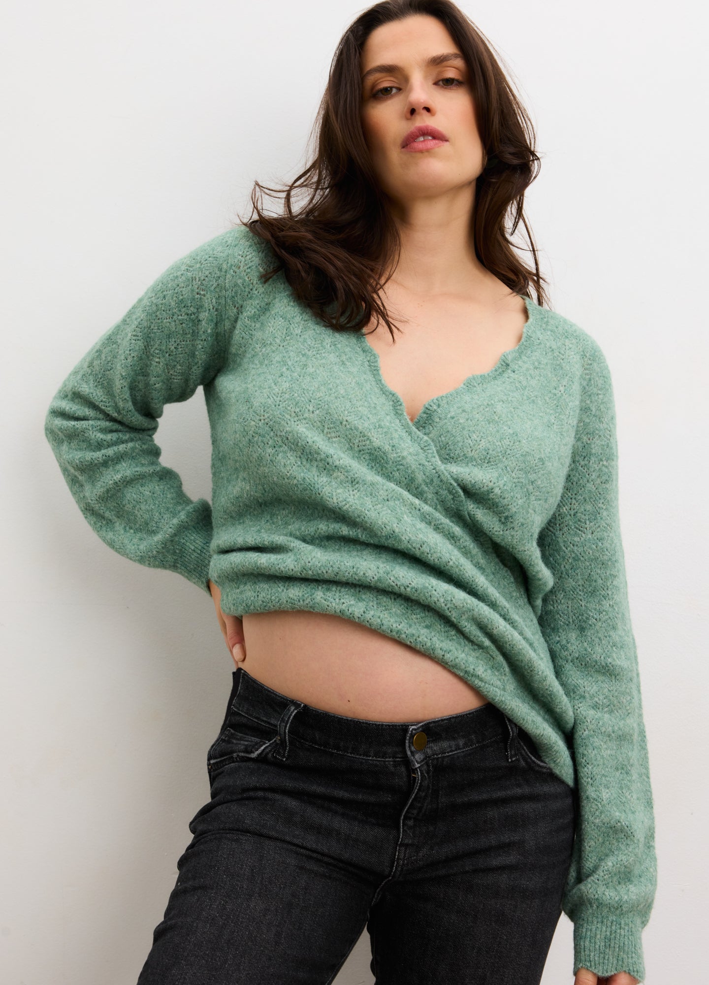 Pregnant woman wearing matcha green pointelle knit maternity sweater with scalloped neckline and long sleeves.
