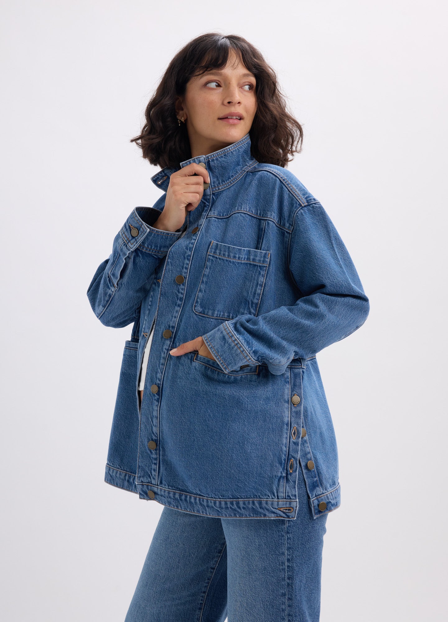 Blue denim maternity utility jacket with button front, chest pockets, and adjustable side tabs.