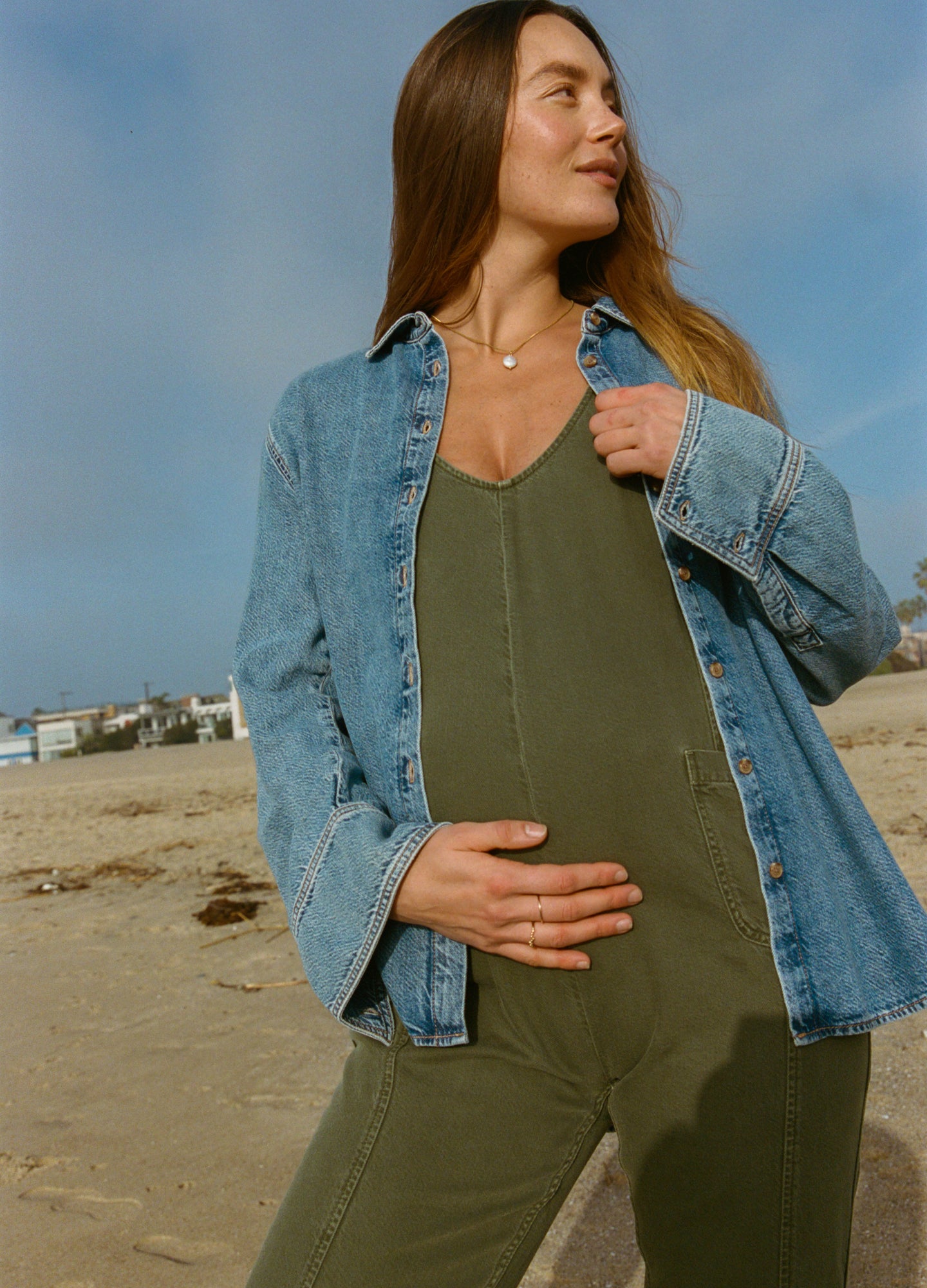 Light blue oversized denim jacket layered over olive green sleeveless maternity jumpsuit with a relaxed fit.