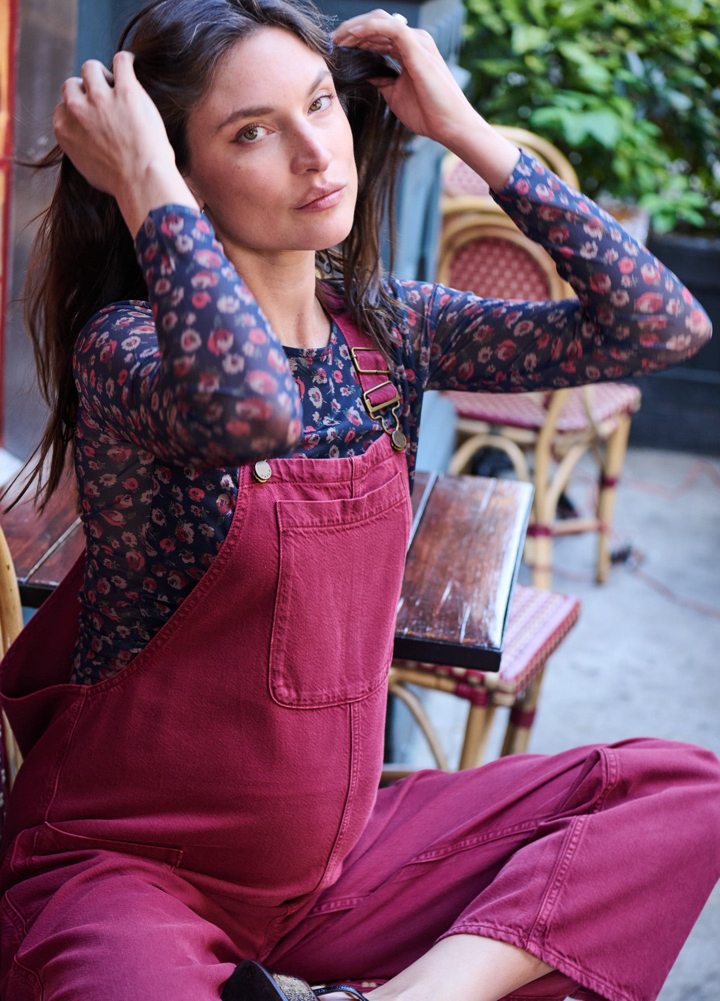 Rose-colored maternity denim overalls with adjustable straps and a front pocket, worn over a floral long-sleeve top.