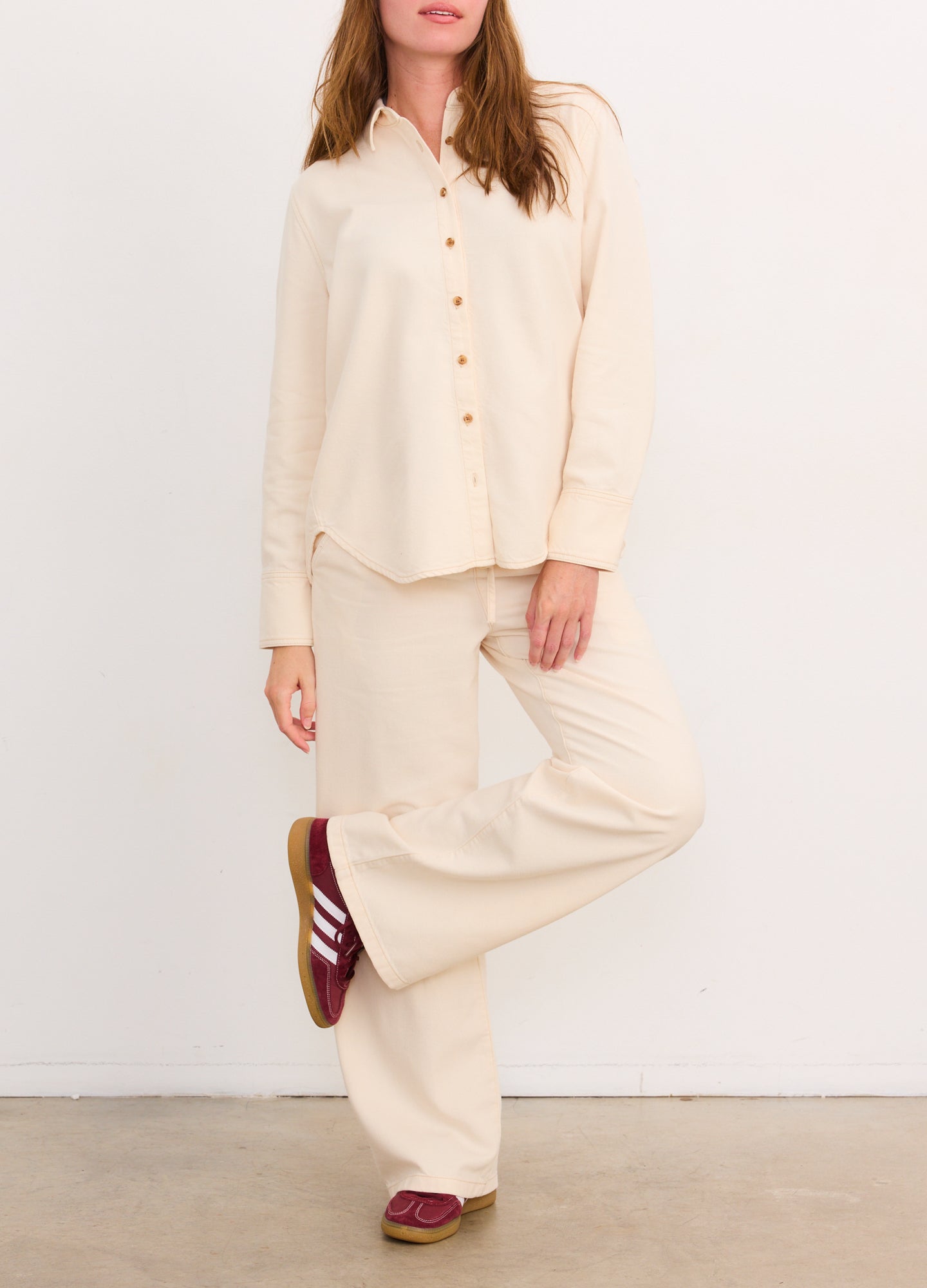 Cream-colored drapey wide-leg maternity denim pants paired with matching button-up shirt and burgundy sneakers.