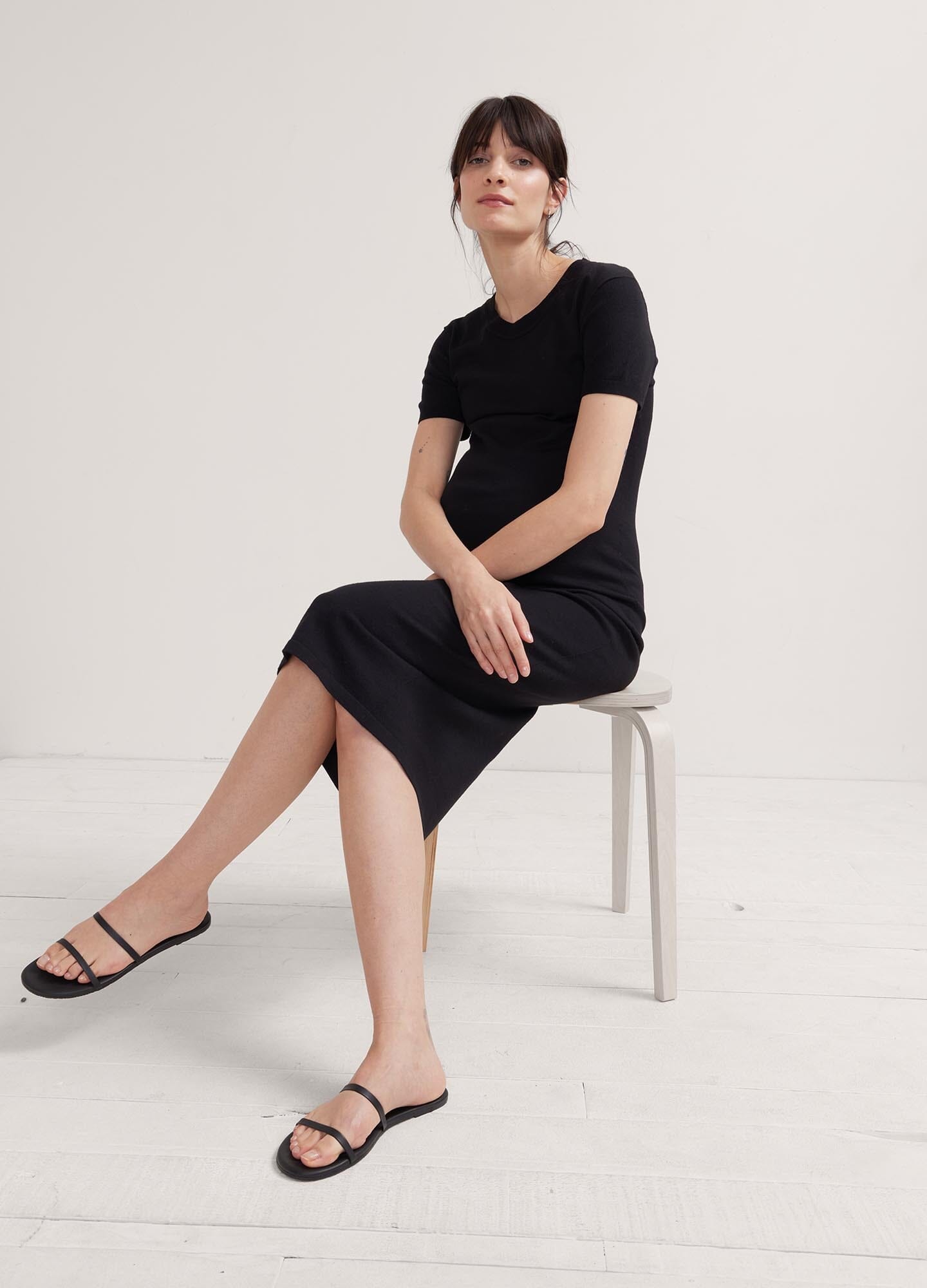 The Eliza Dress POS - Black short-sleeve maternity dress with nursing-friendly design and fitted silhouette, styled with tall black boots.