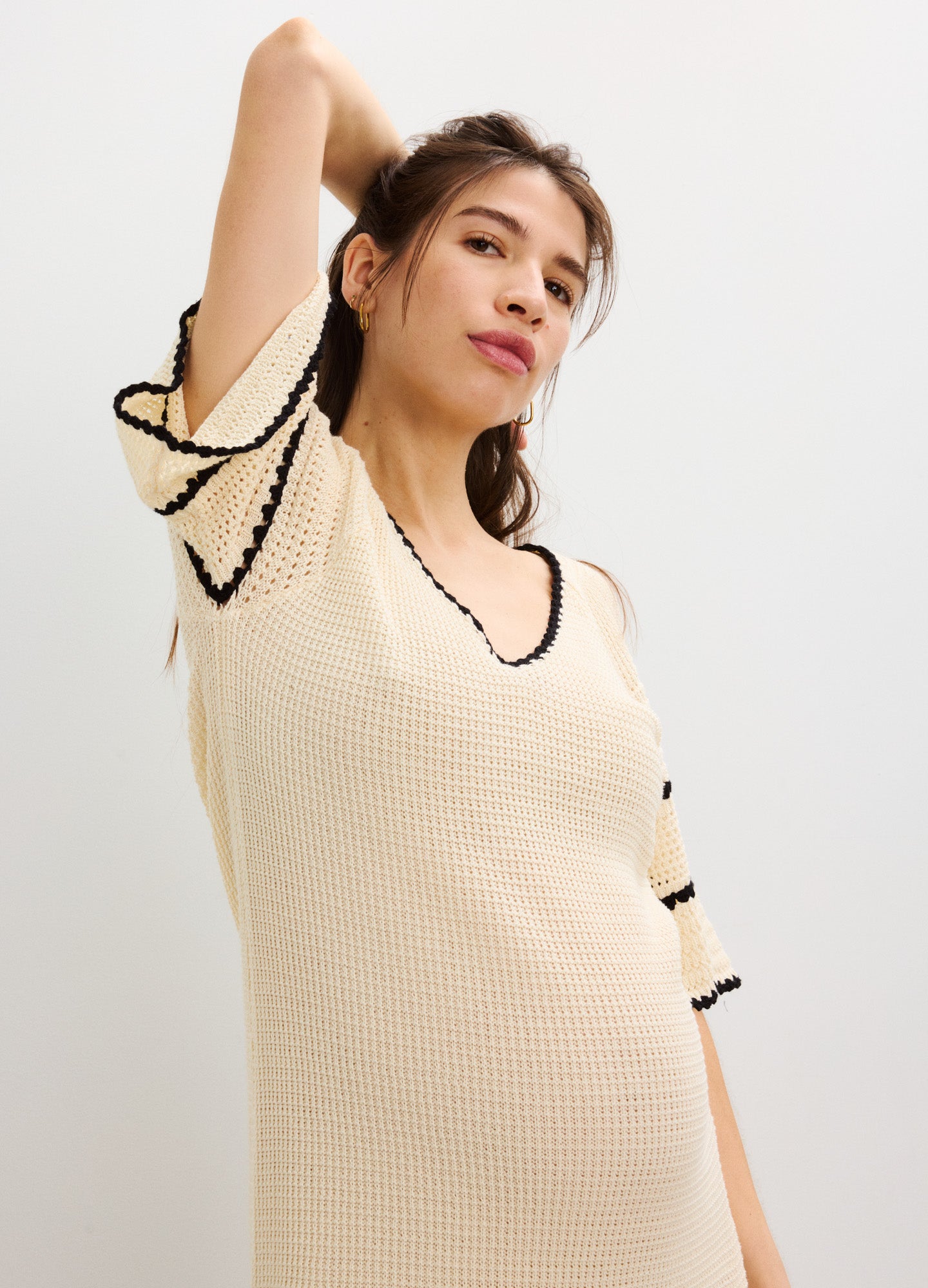 Cream crochet maternity dress with black trim and short flutter sleeves.