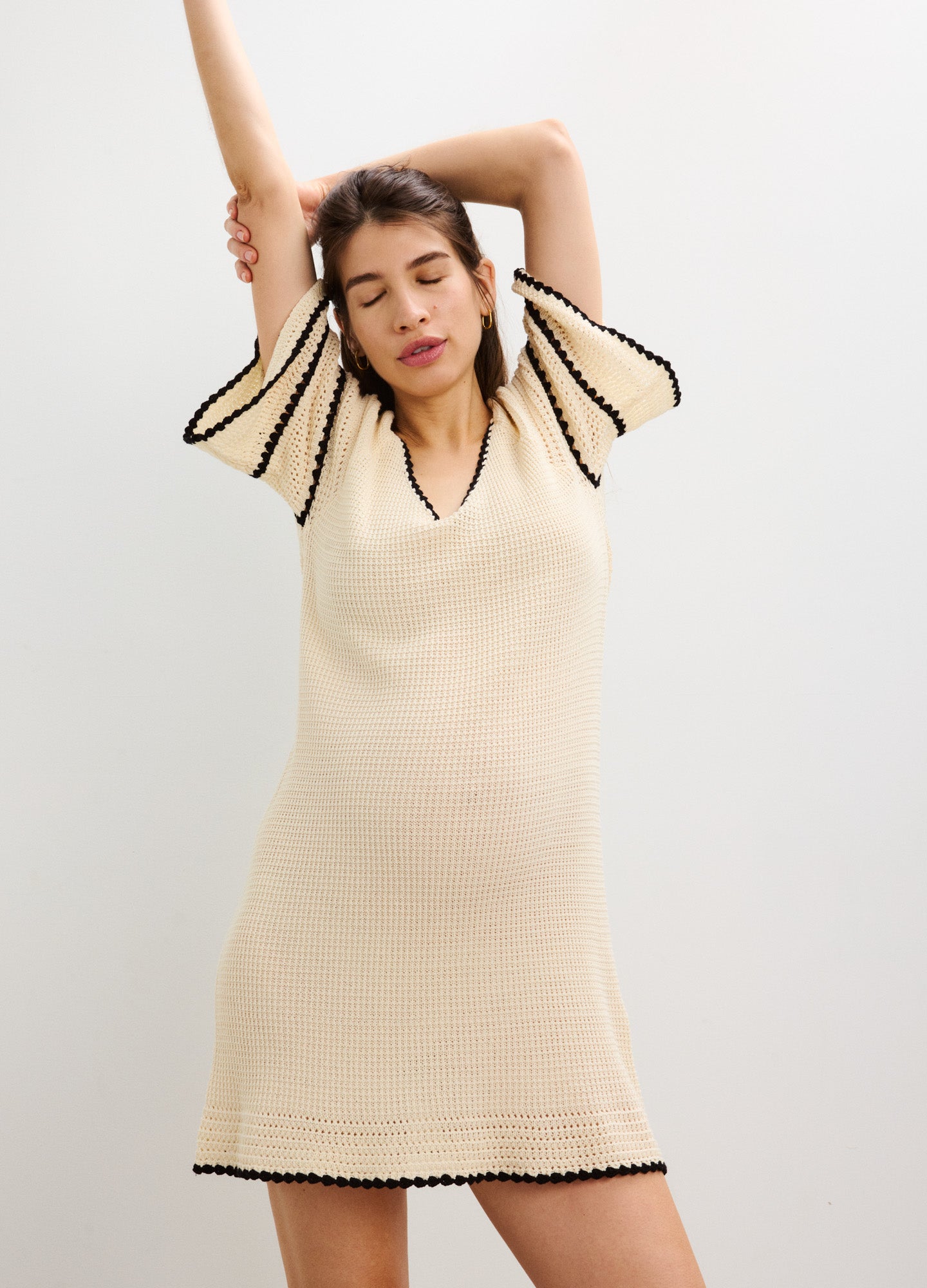 Cream crochet maternity dress with black trim, flutter sleeves, and V-neckline designed for pregnant women.