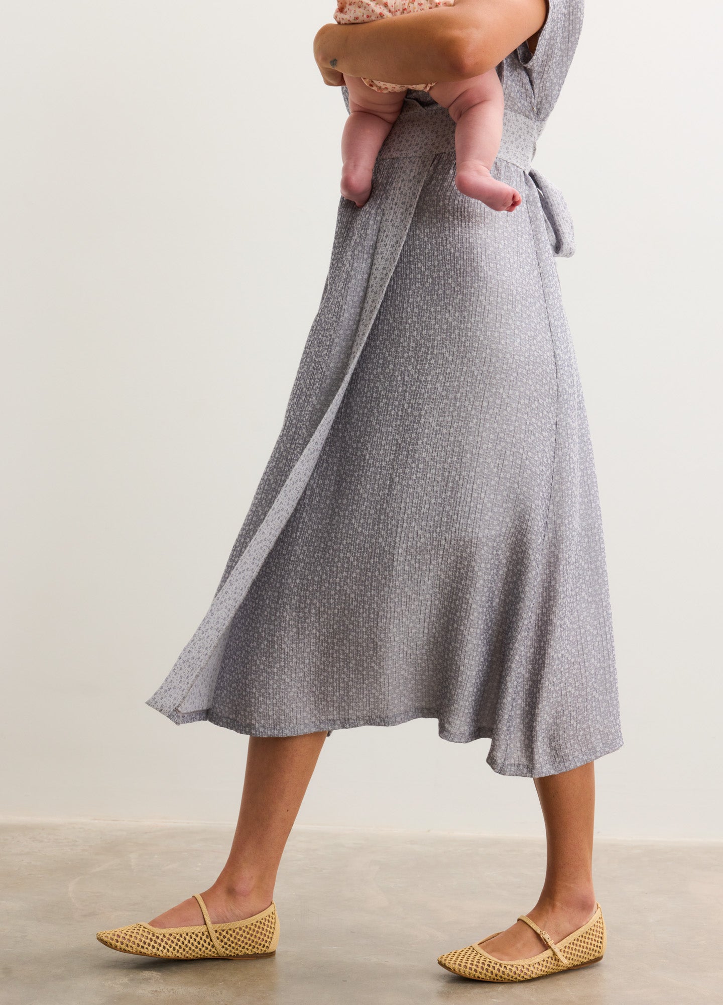 Light gray maternity midi dress with subtle jacquard texture, flowing A-line skirt, and tie waist detail.