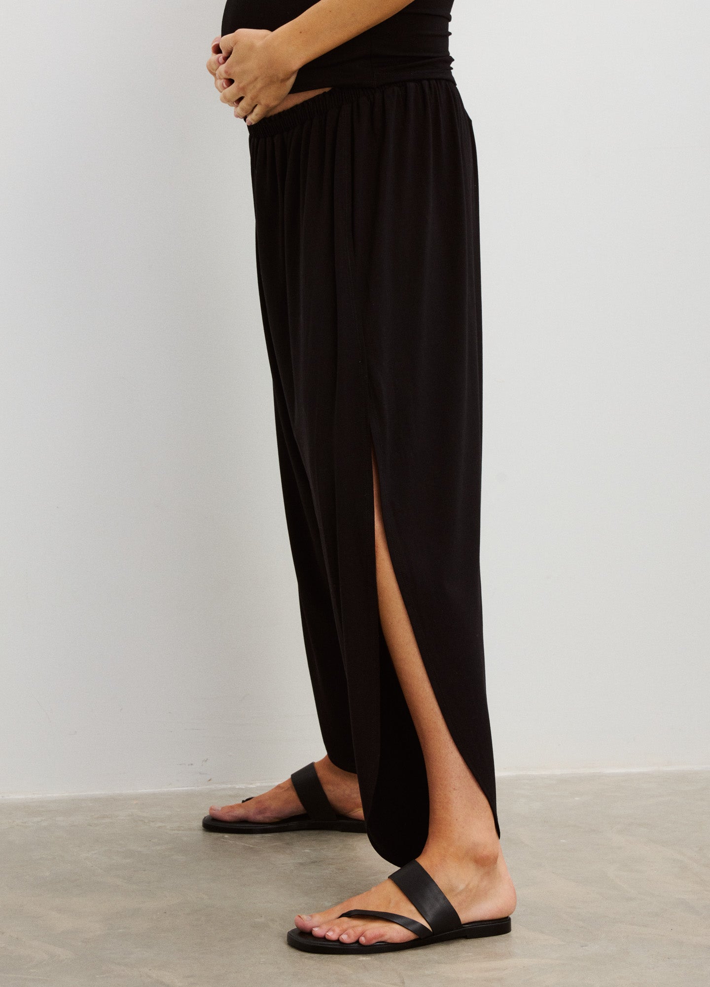 Black maternity pants with a high, stretchy waistband and side leg slits, styled for pregnant comfort.