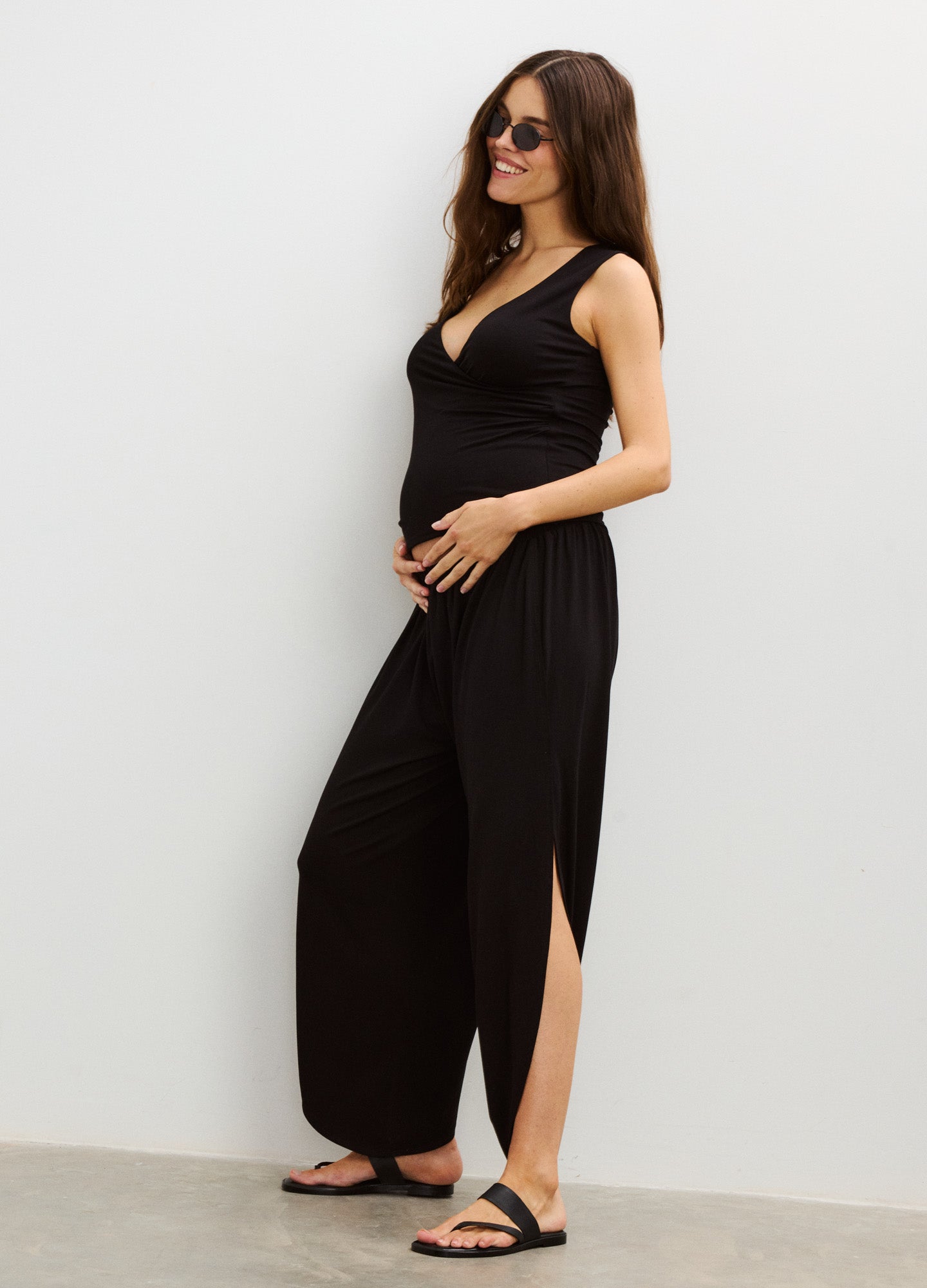 Black maternity pants with side slits and a relaxed fit, worn with a sleeveless black top and sandals.