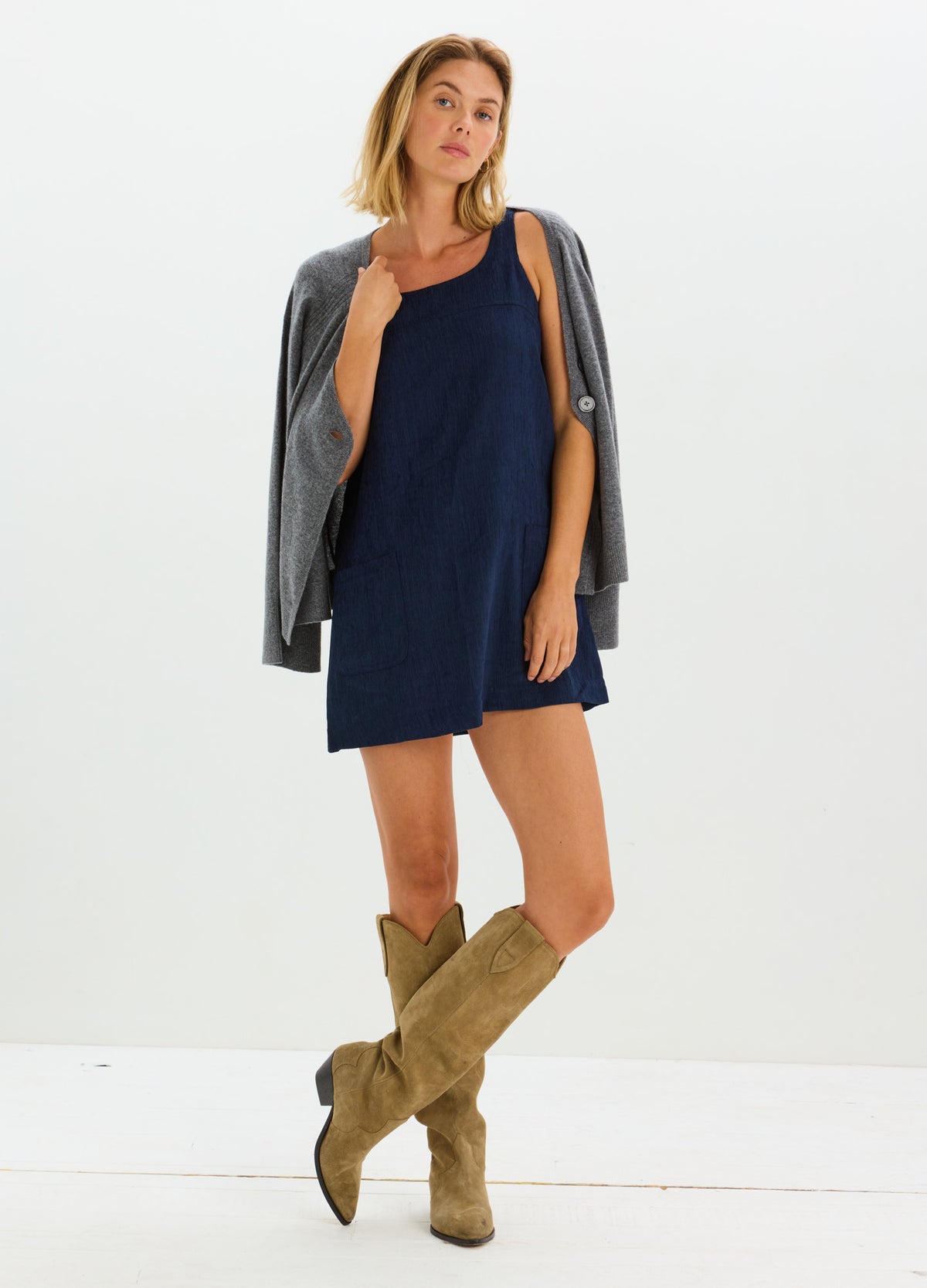 Navy blue maternity mini dress in soft corduroy with sleeveless design and loose fit paired with tan slouchy knee-high boots
