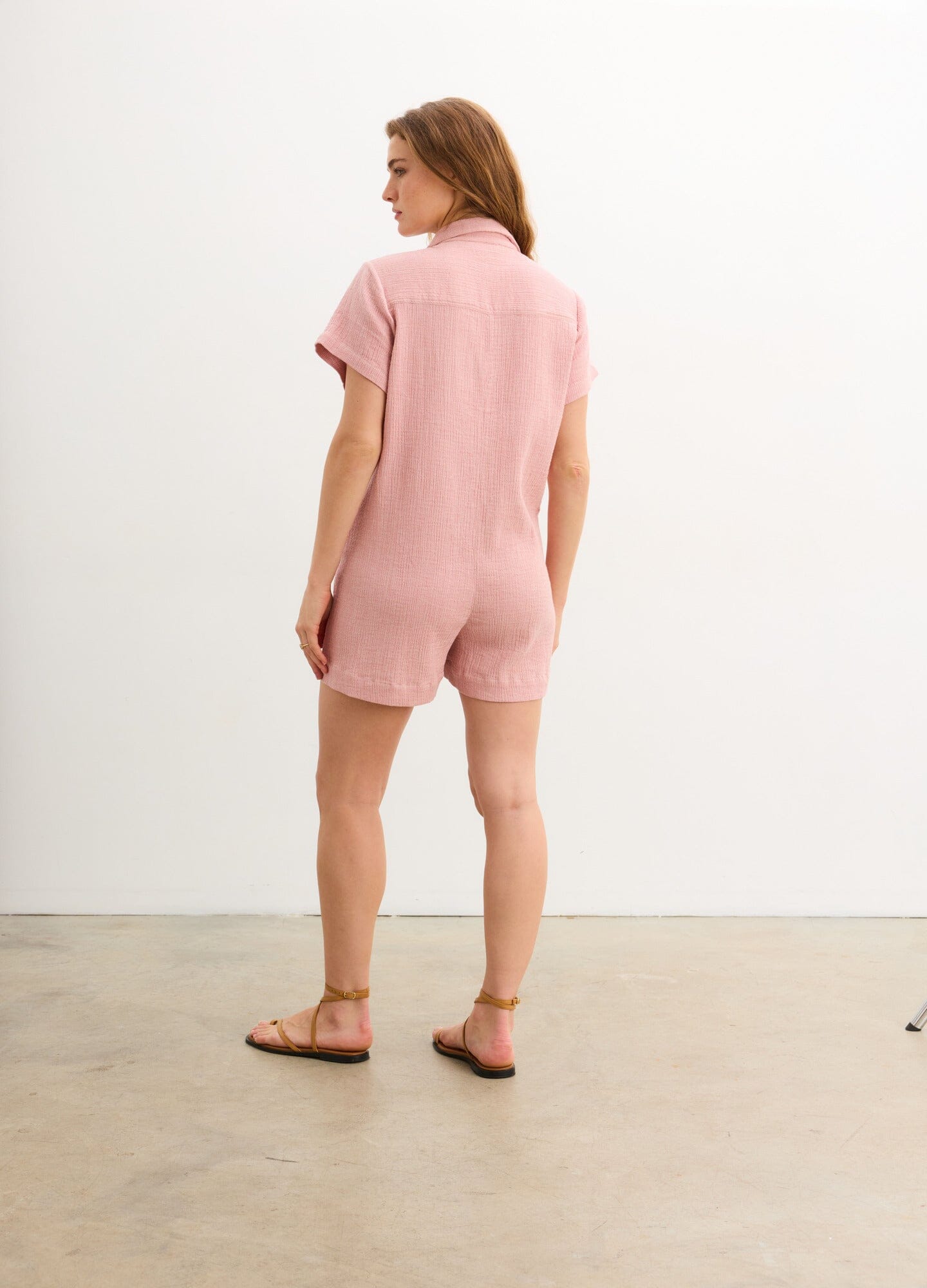 The Lenora Romper - Soft pink short-sleeve maternity romper with button front and side pockets, designed for nursing and postpartum comfort.