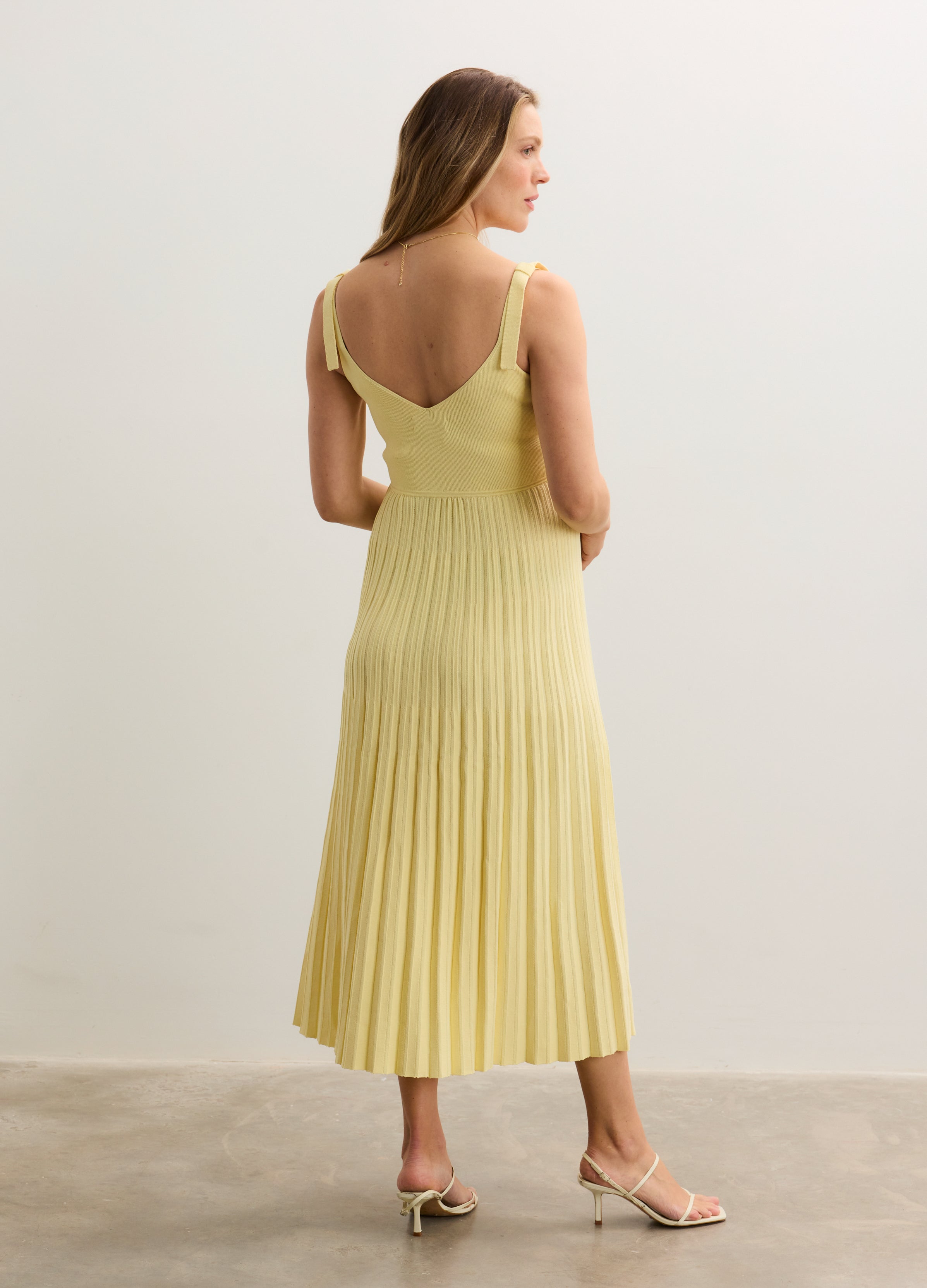 Soft yellow sleeveless midi dress with pleated skirt and low V-back, worn by pregnant model.
