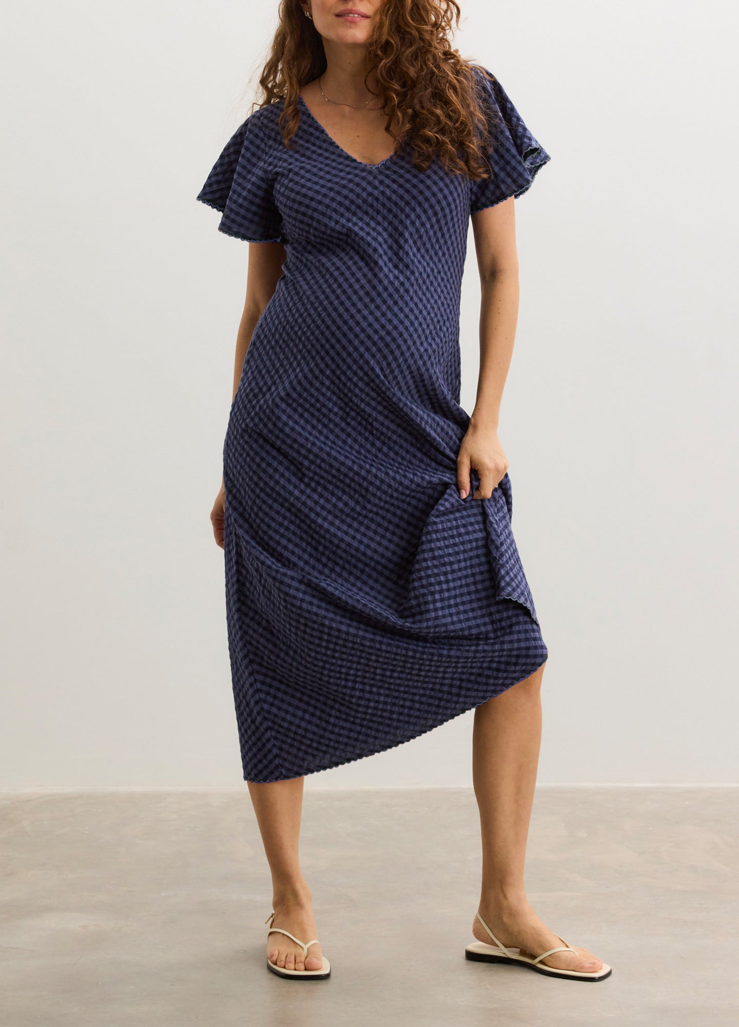 Navy blue maternity dress with white polka dots, flutter sleeves, and V-neckline, midi length.