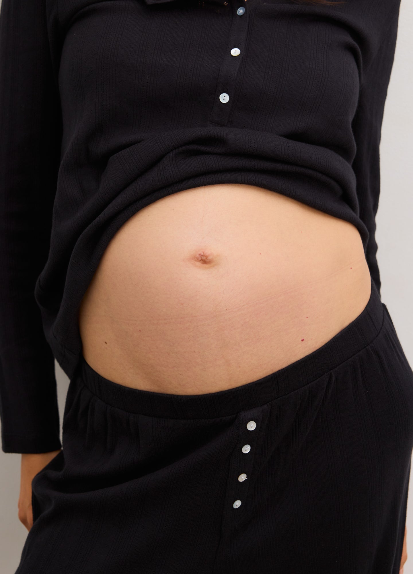 Black maternity pants with button details, designed for pregnant comfort and stretch.