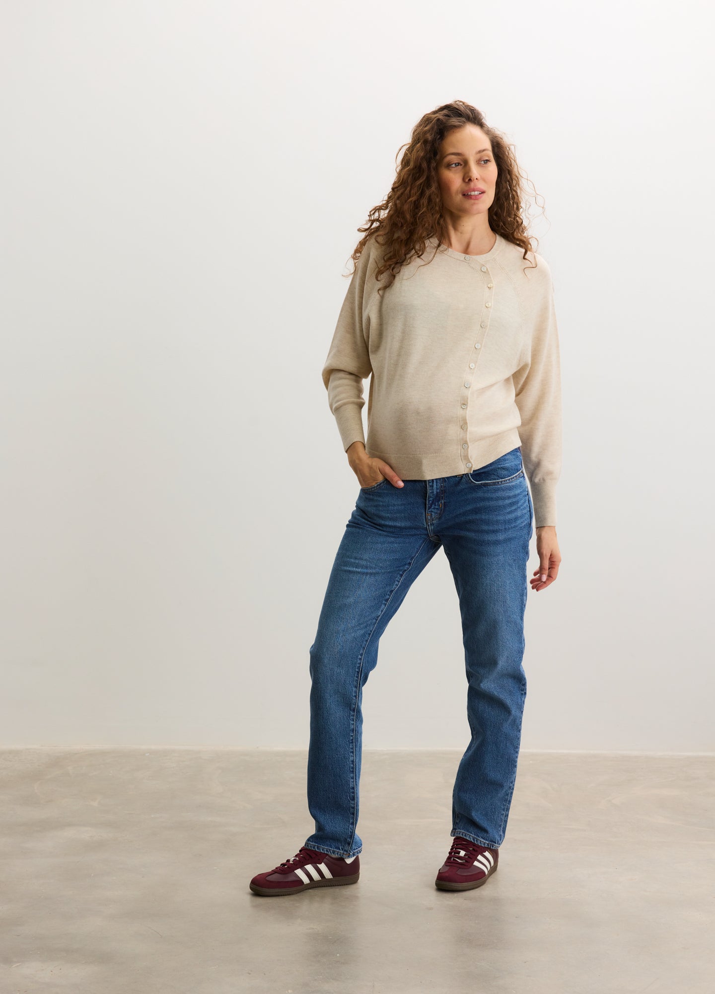 Beige maternity cardigan with button front, long sleeves, and relaxed fit paired with blue jeans and red sneakers.
