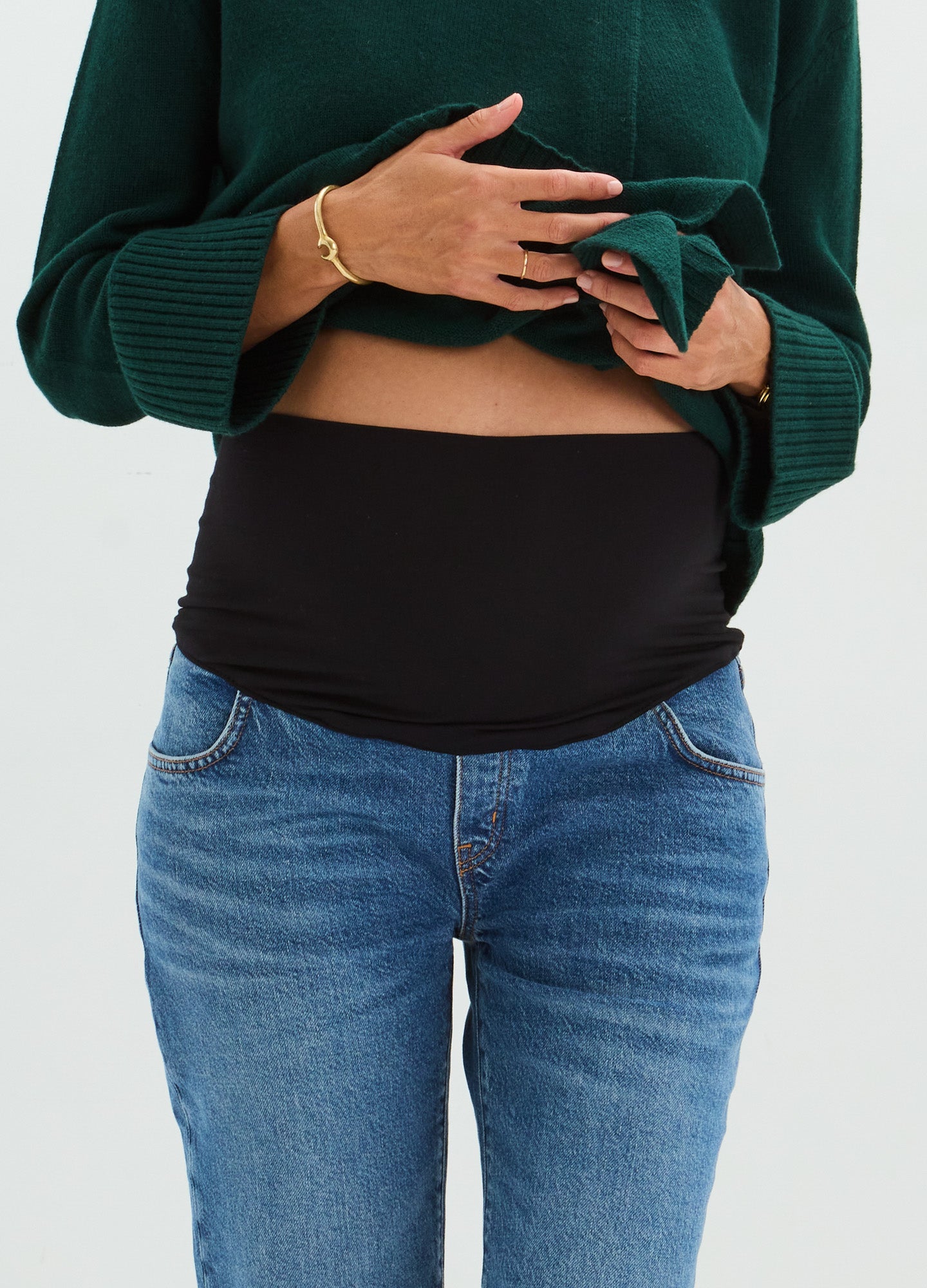 Blue straight-leg denim maternity jeans with black over-the-bump stretchy panel and a green sweater.