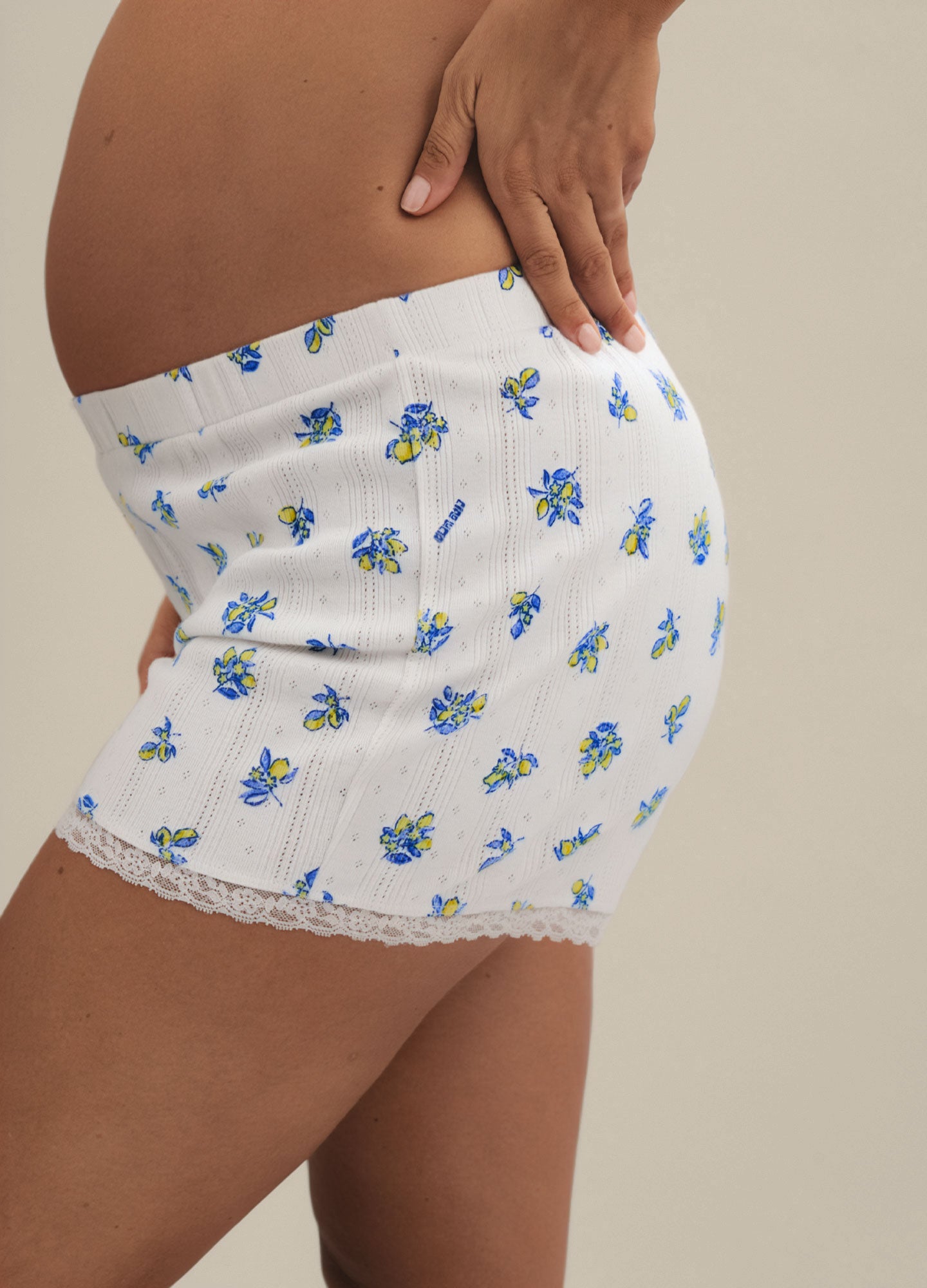 White knit maternity lounge shorts with blue floral pointelle pattern and lace trim on hem.