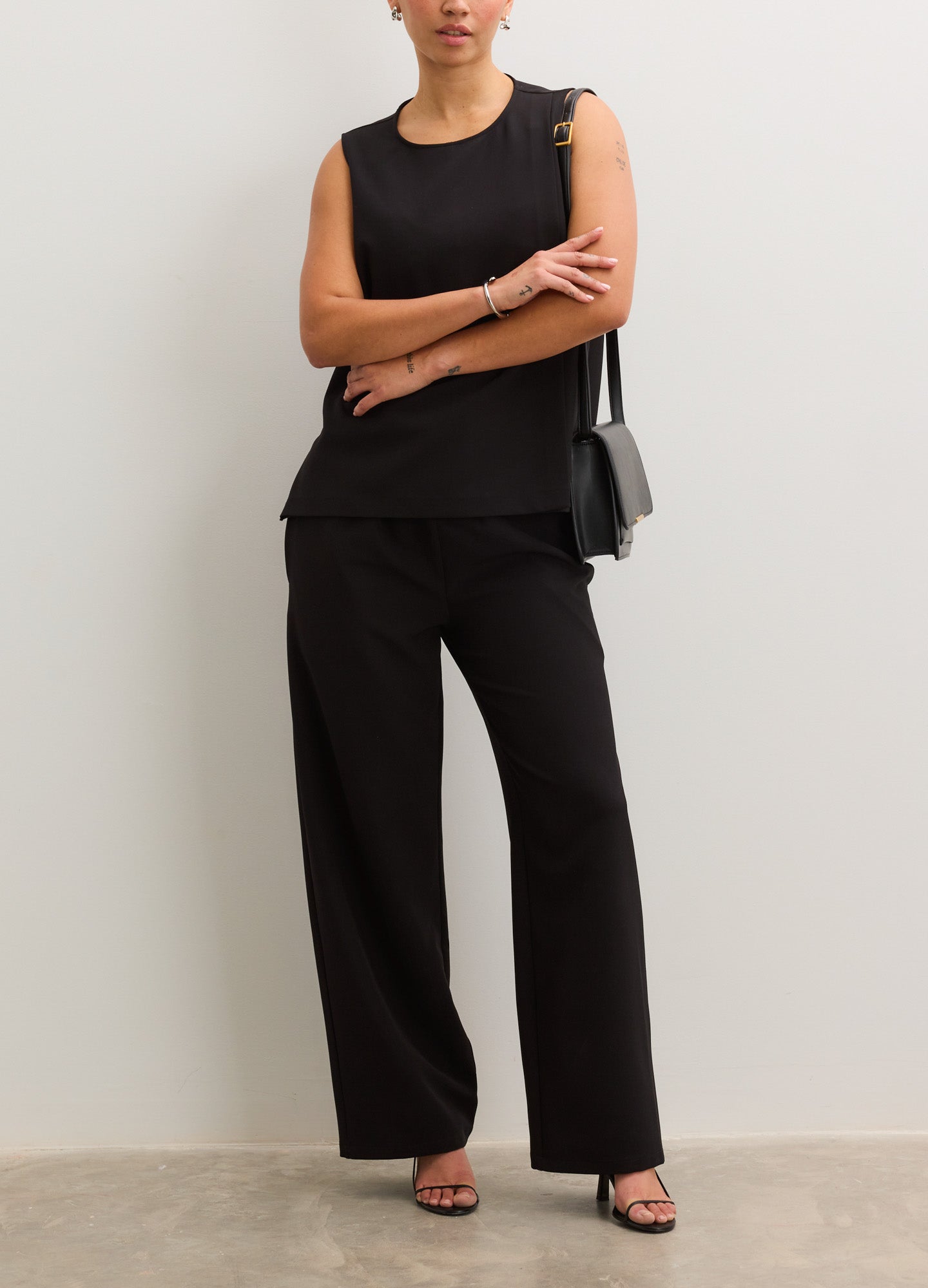 Black maternity pants with a relaxed straight-leg fit, worn with a sleeveless black top and black sandals.
