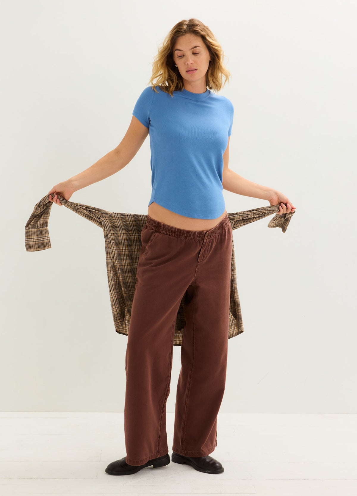 Light blue fitted ribbed maternity tee with short sleeves styled with loose brown pants and a plaid shirt.