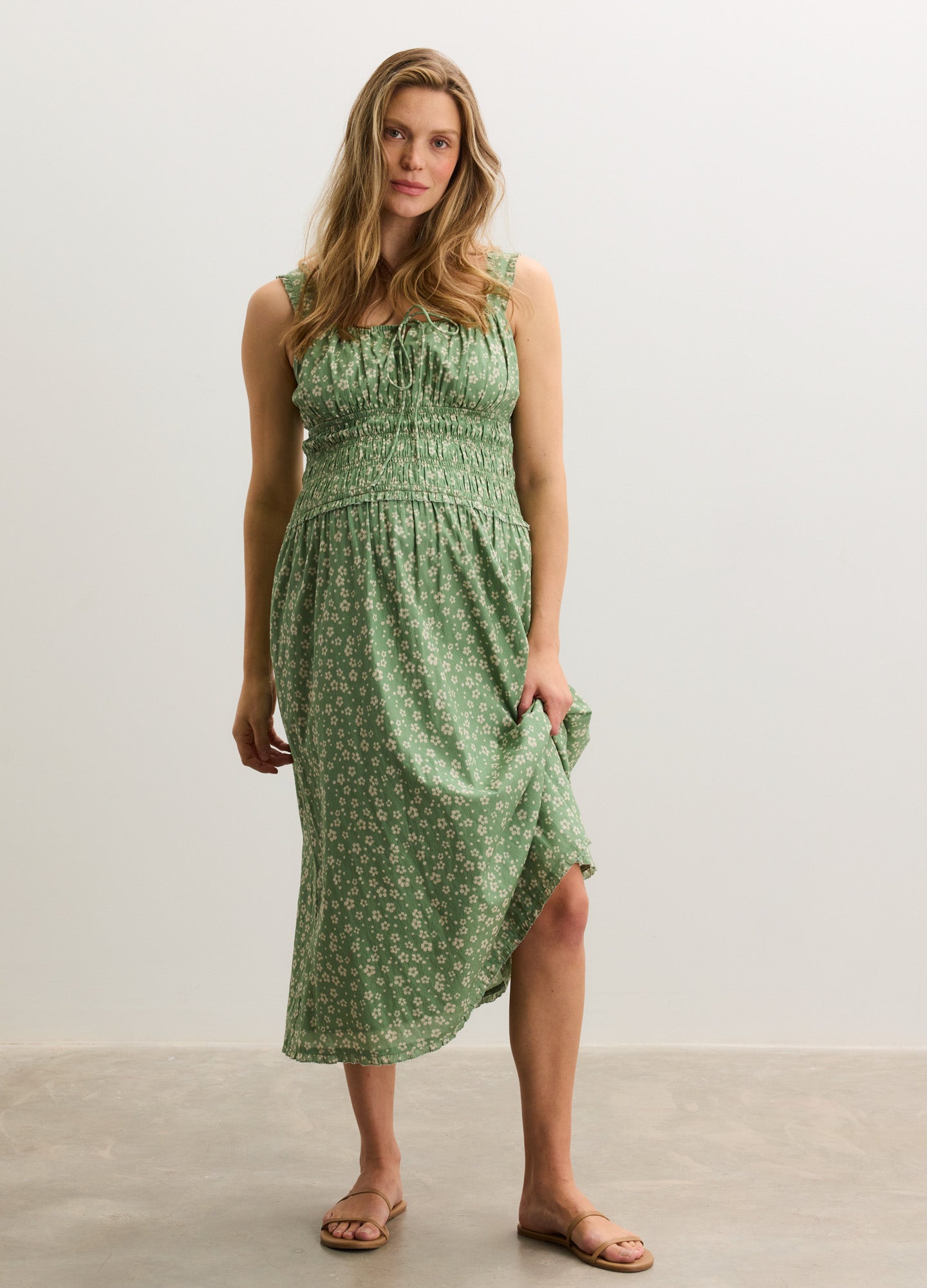 Light green sleeveless maternity dress with small white floral print and smocked bodice, midi length.