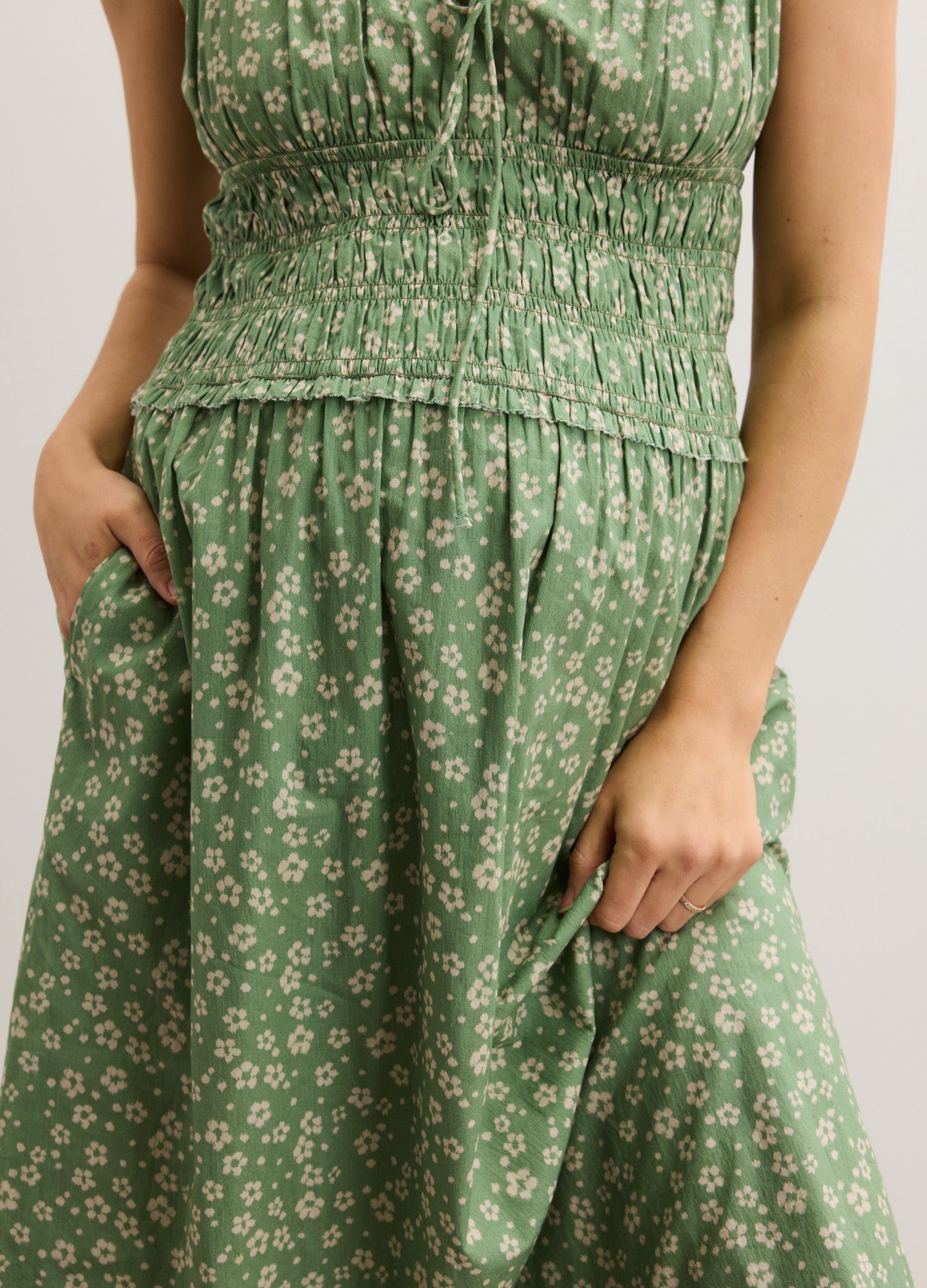 Green floral maternity dress with smocked bodice and gathered waist, sleeveless design.