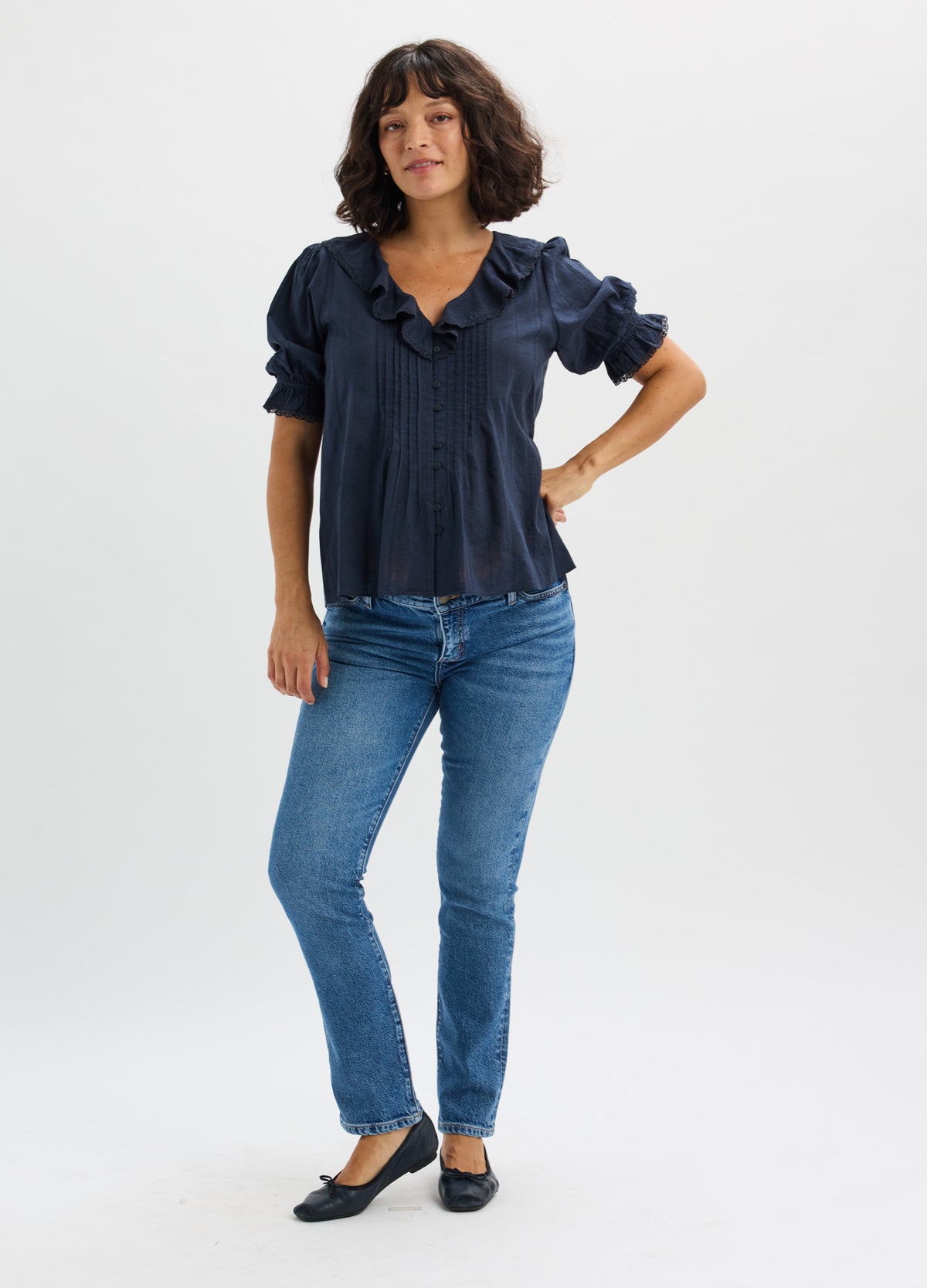 Blue slim-fit maternity jeans with stretch fabric modeled with a dark navy blouse and black flats.