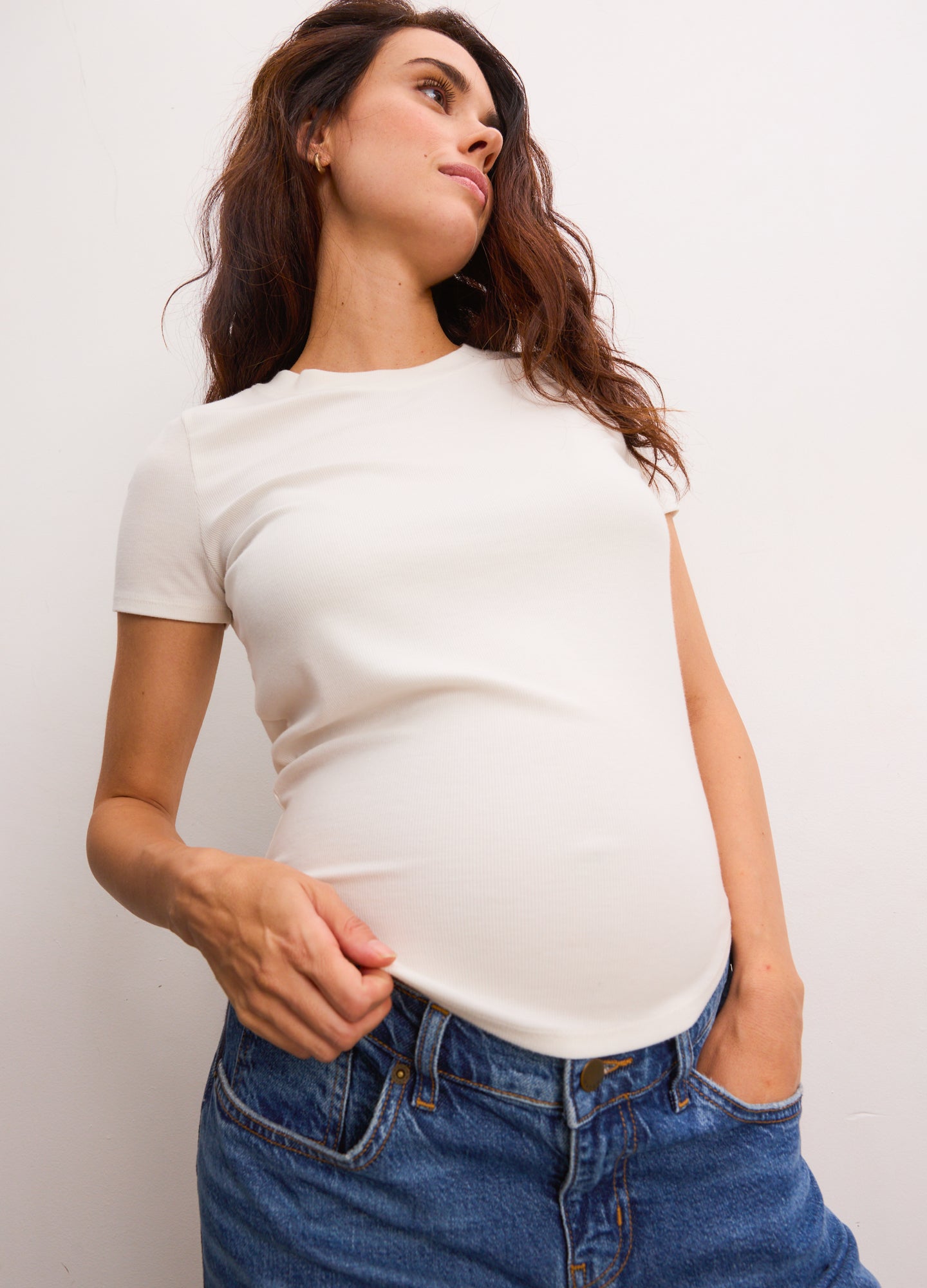 Cream-colored ribbed short-sleeve maternity tee with a fitted silhouette on a pregnant model.