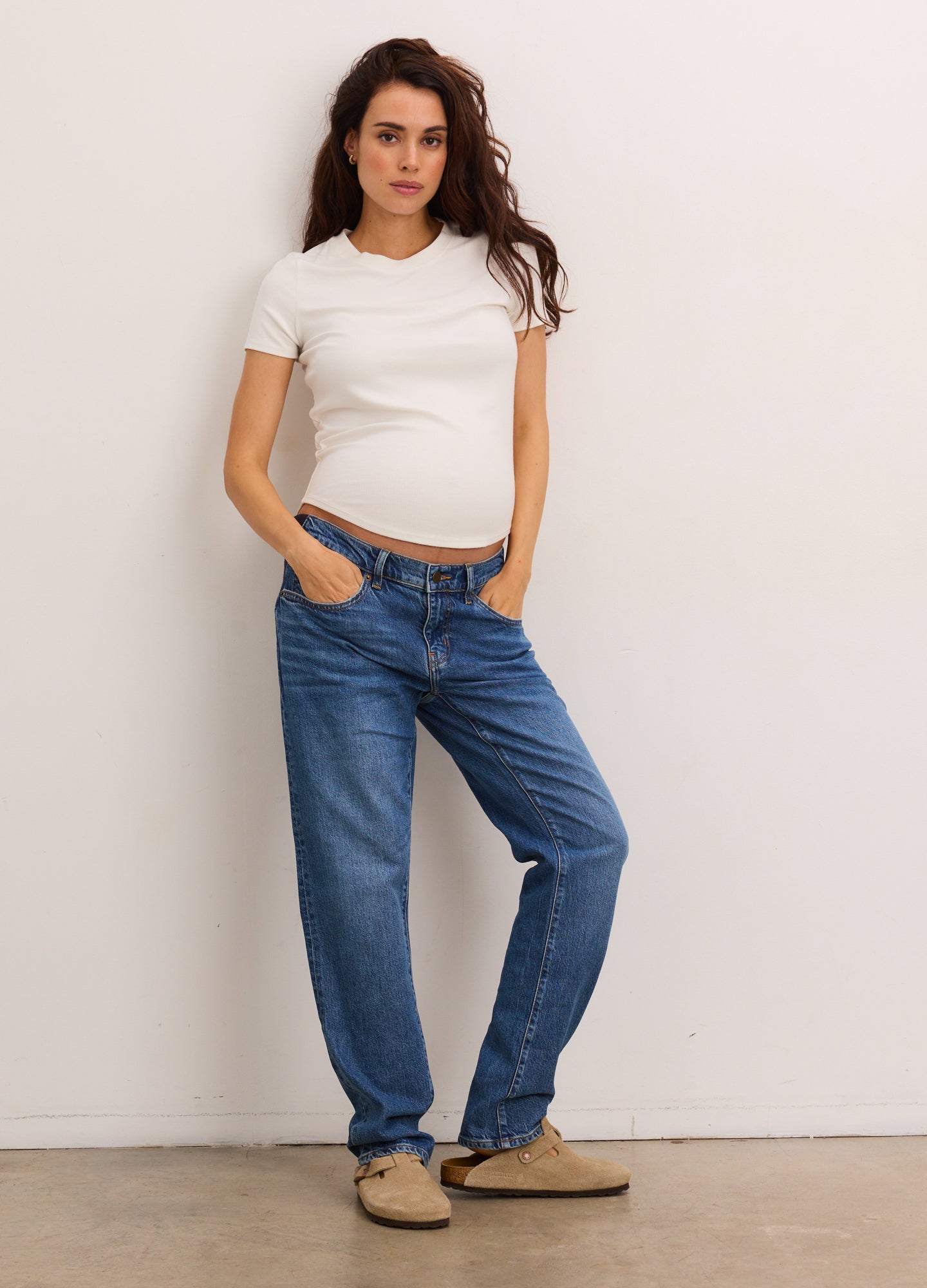 White fitted short-sleeve maternity top paired with relaxed blue denim jeans and tan slip-on shoes.