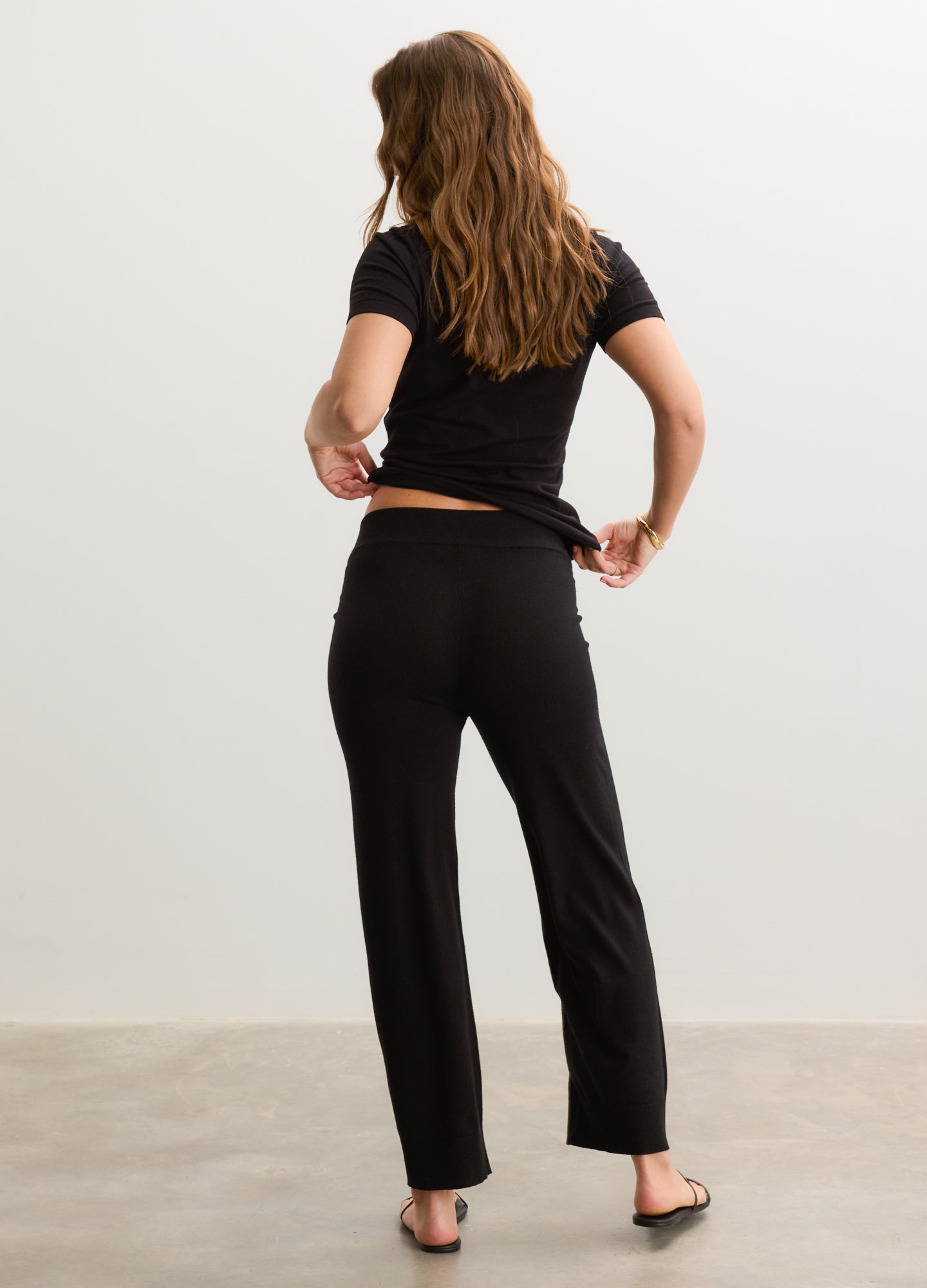 Black soft knit maternity crop pants with a relaxed fit, worn by a pregnant model from the back.