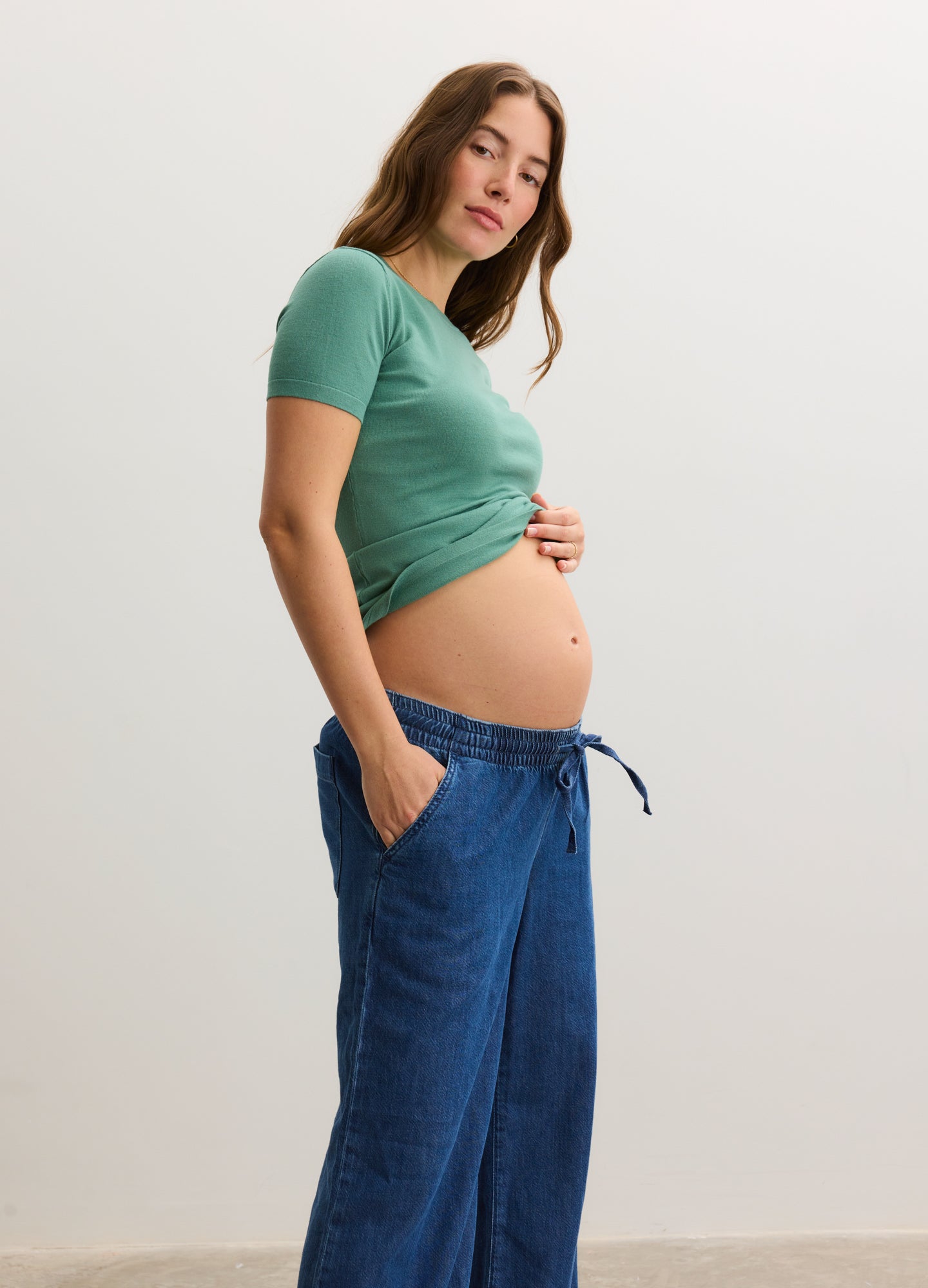 Mint green short-sleeve knit maternity tee with ruched sides, modeled with dark blue drawstring maternity pants.